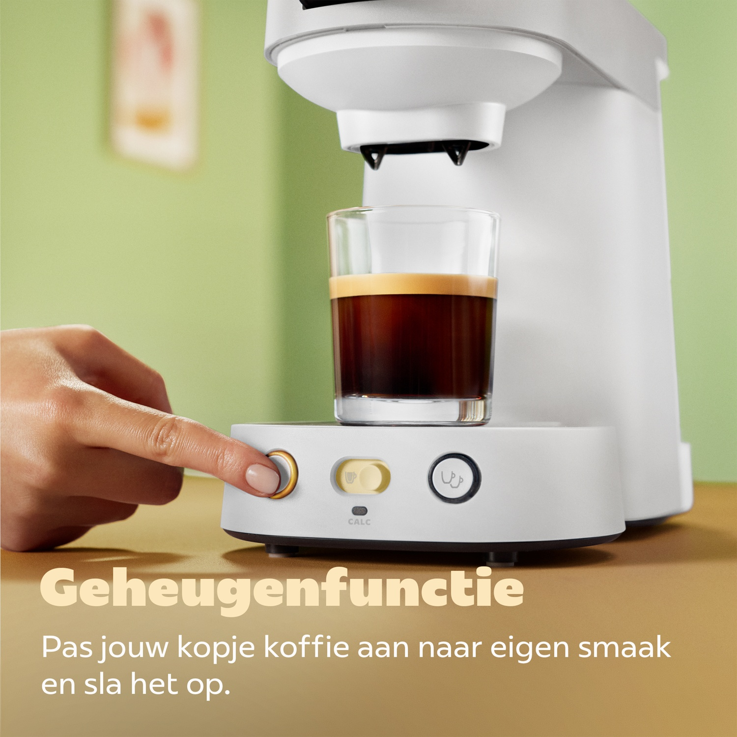 Hand drukt op een gouden knop op een wit koffiezetapparaat met een glas koffie.