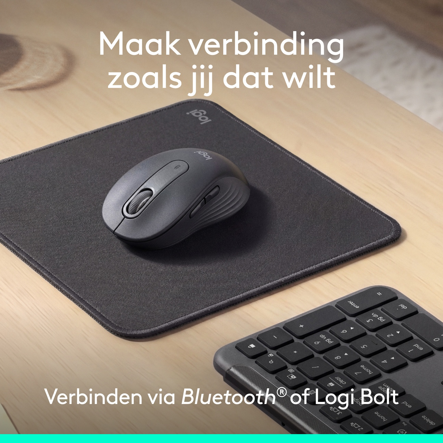 Une souris d'ordinateur grise et un tapis de souris sur un bureau en bois près d'un clavier.