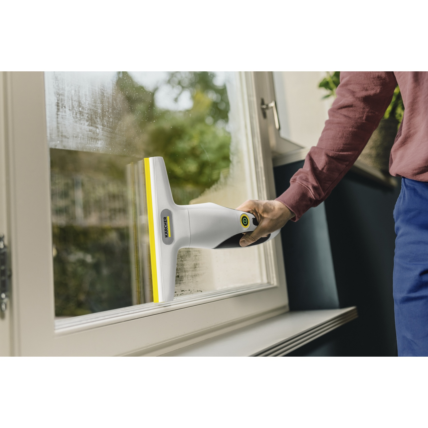 Une personne utilise un aspirateur de vitres Kärcher blanc et jaune pour nettoyer une vitre.