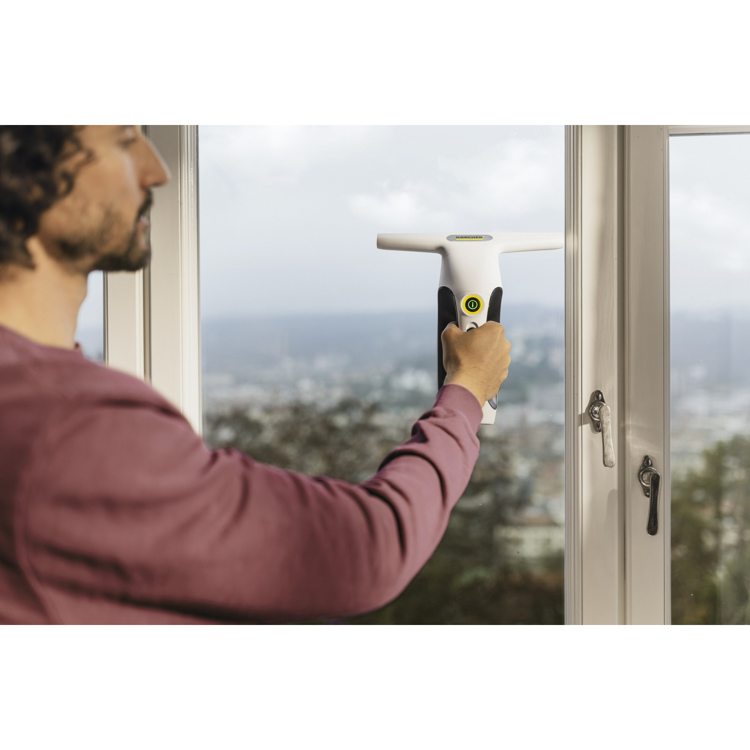 Un homme nettoie une vitre avec un aspirateur de vitres Kärcher.