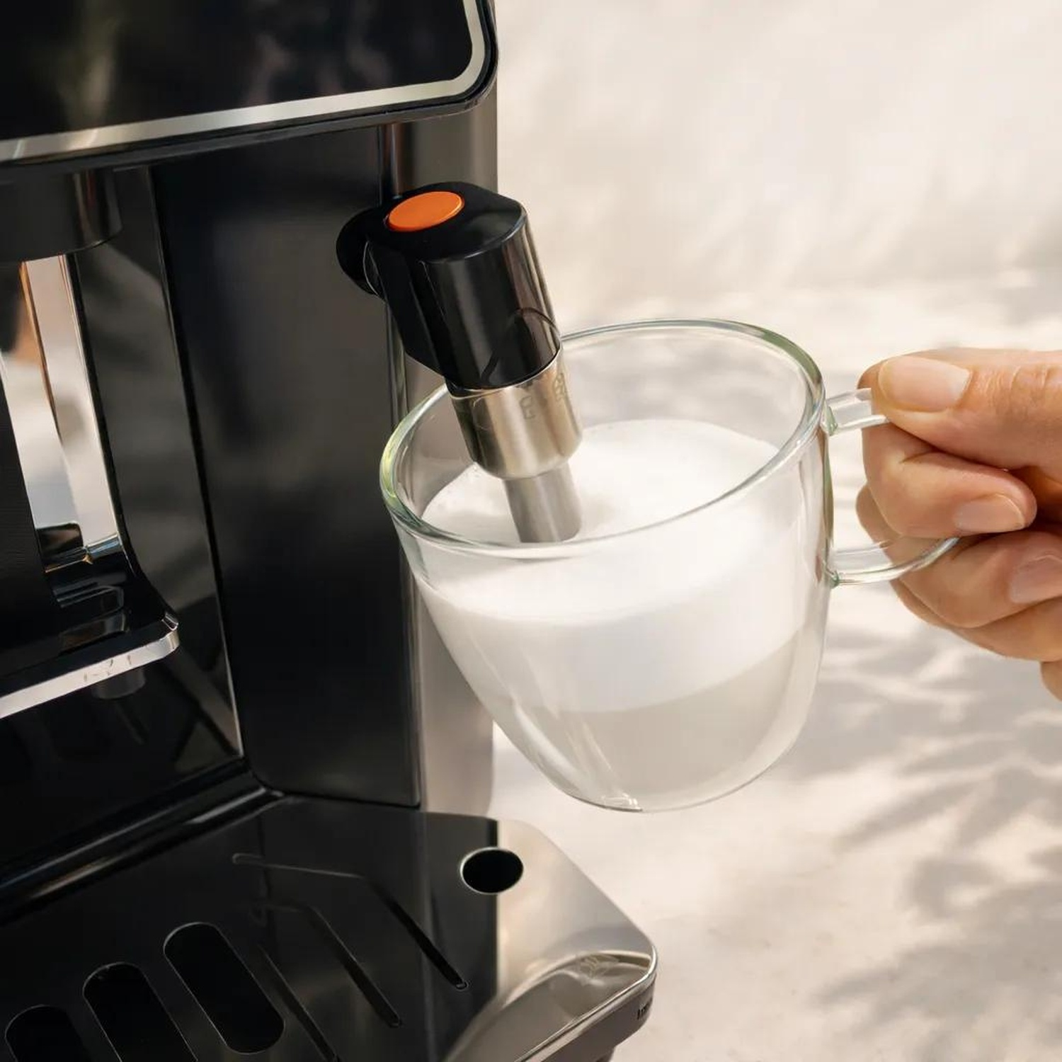 Une main tient une tasse en verre pendant qu'un mousseur verse de la mousse.