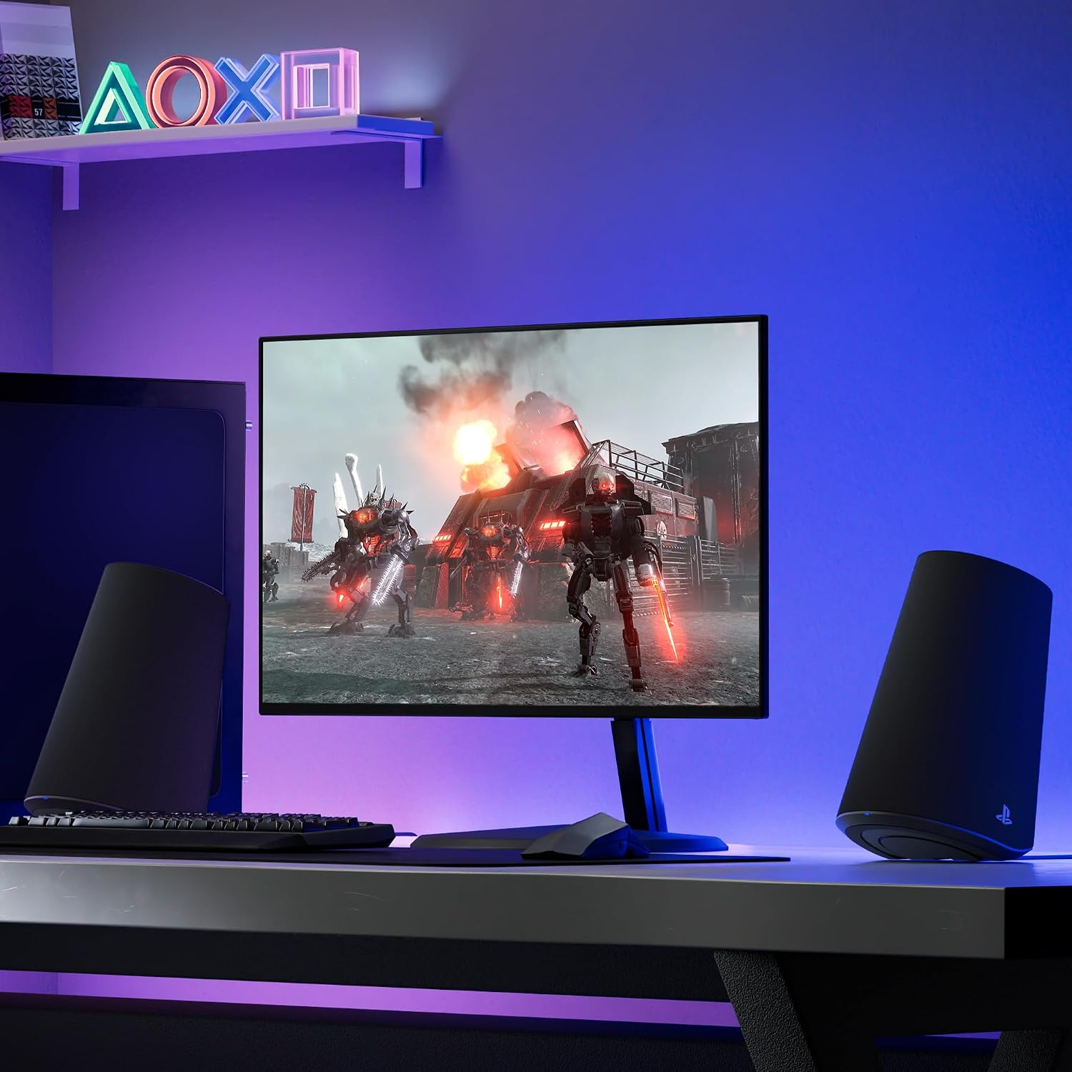 Scrivania da gioco con monitor che mostra un videogioco, affiancato da altoparlanti sotto i simboli PlayStation illuminati.