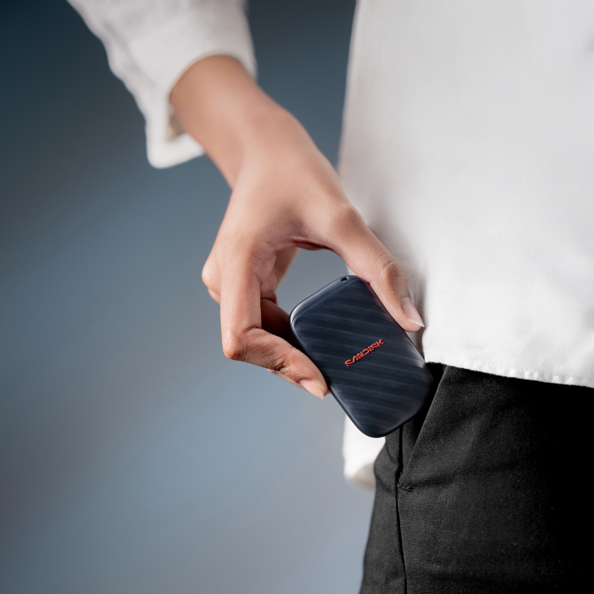 Persona con camisa blanca guarda un SSD SanDisk negro en el bolsillo.