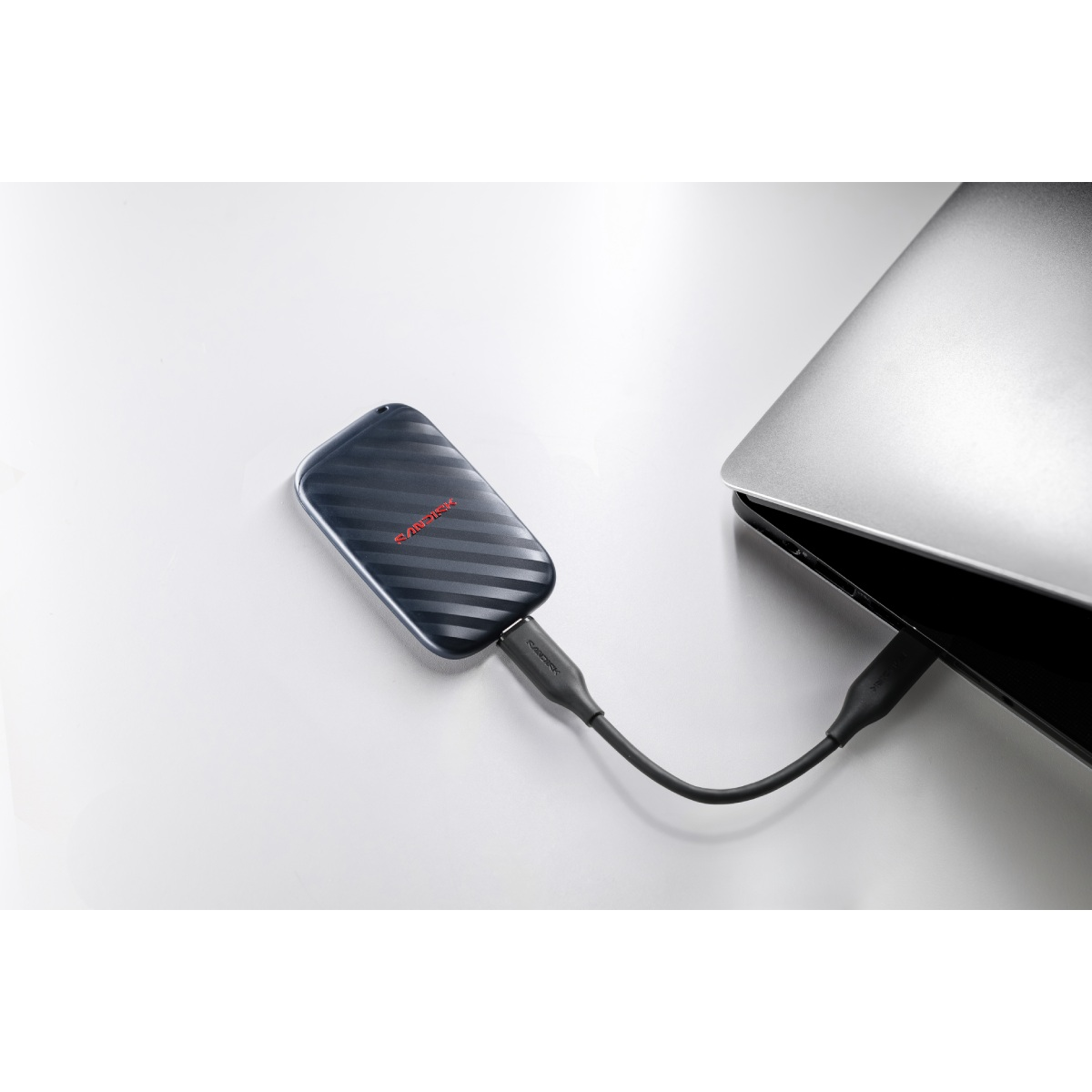 Un SSD SanDisk negro sobre una superficie blanca, conectado por un cable a un ordenador portátil.