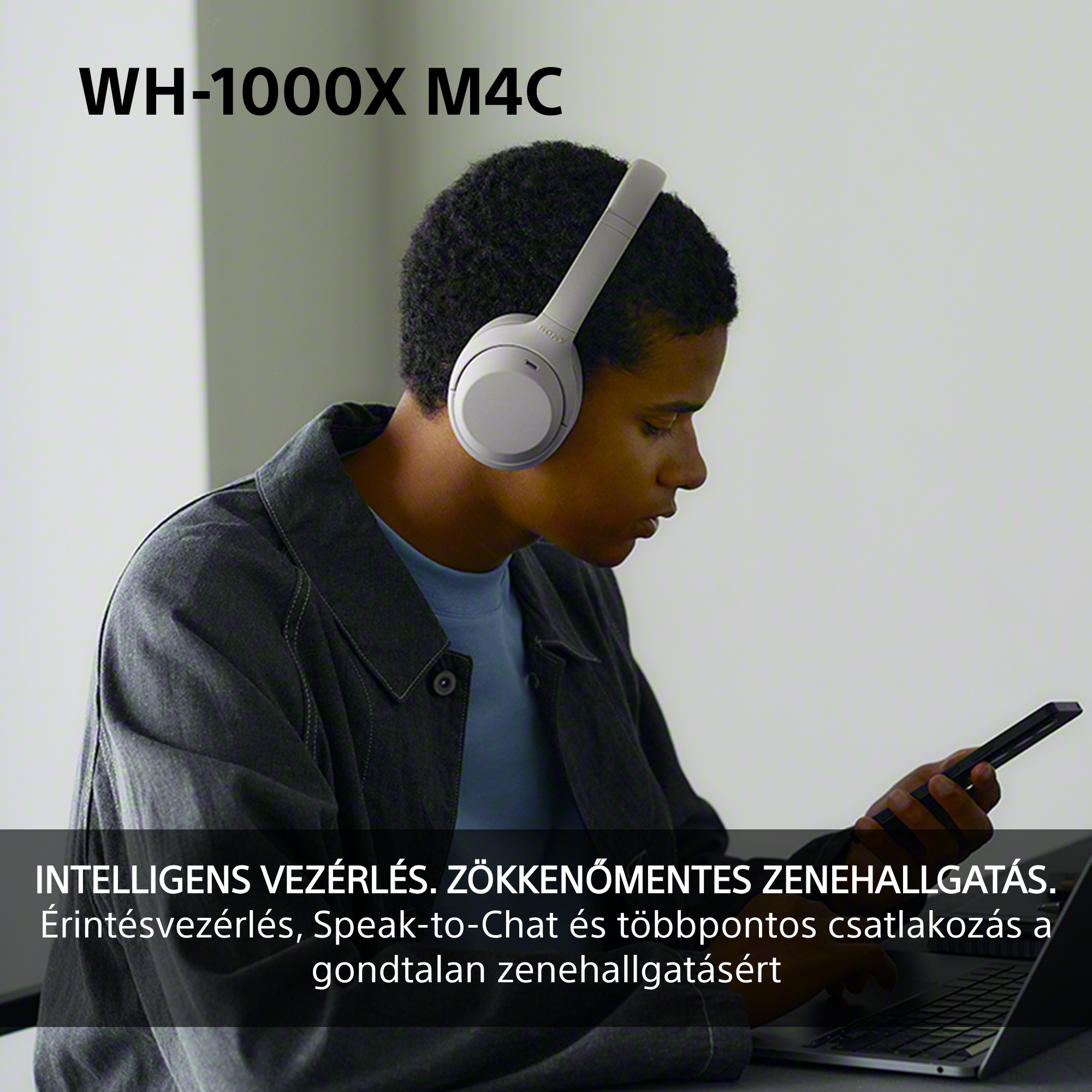 Szürke fejhallgatót viselő fiatalember dolgozik laptopon, okostelefont tart, szöveges feliratokkal.