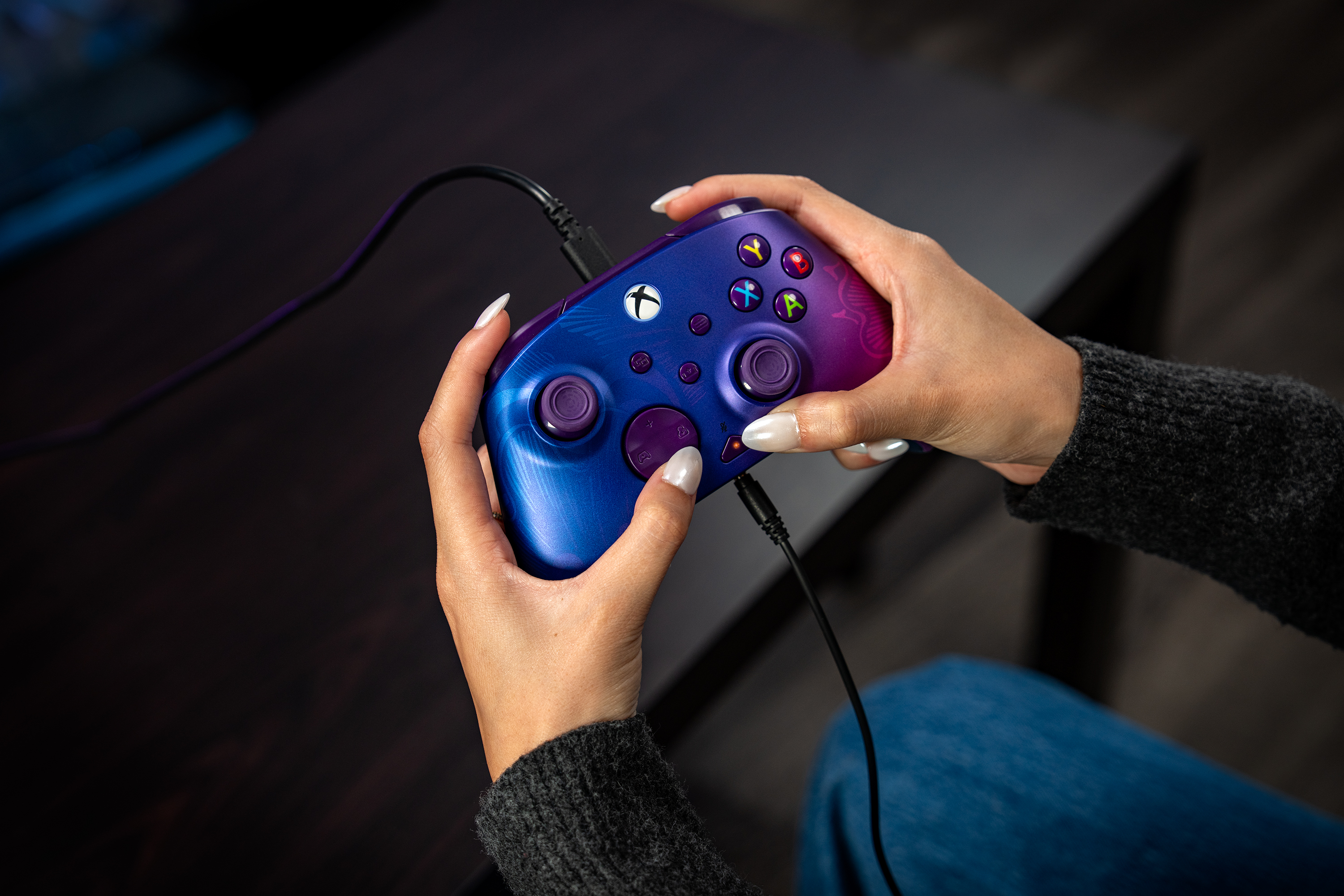 Personne tenant une manette Xbox bleue et violette avec un câble connecté.