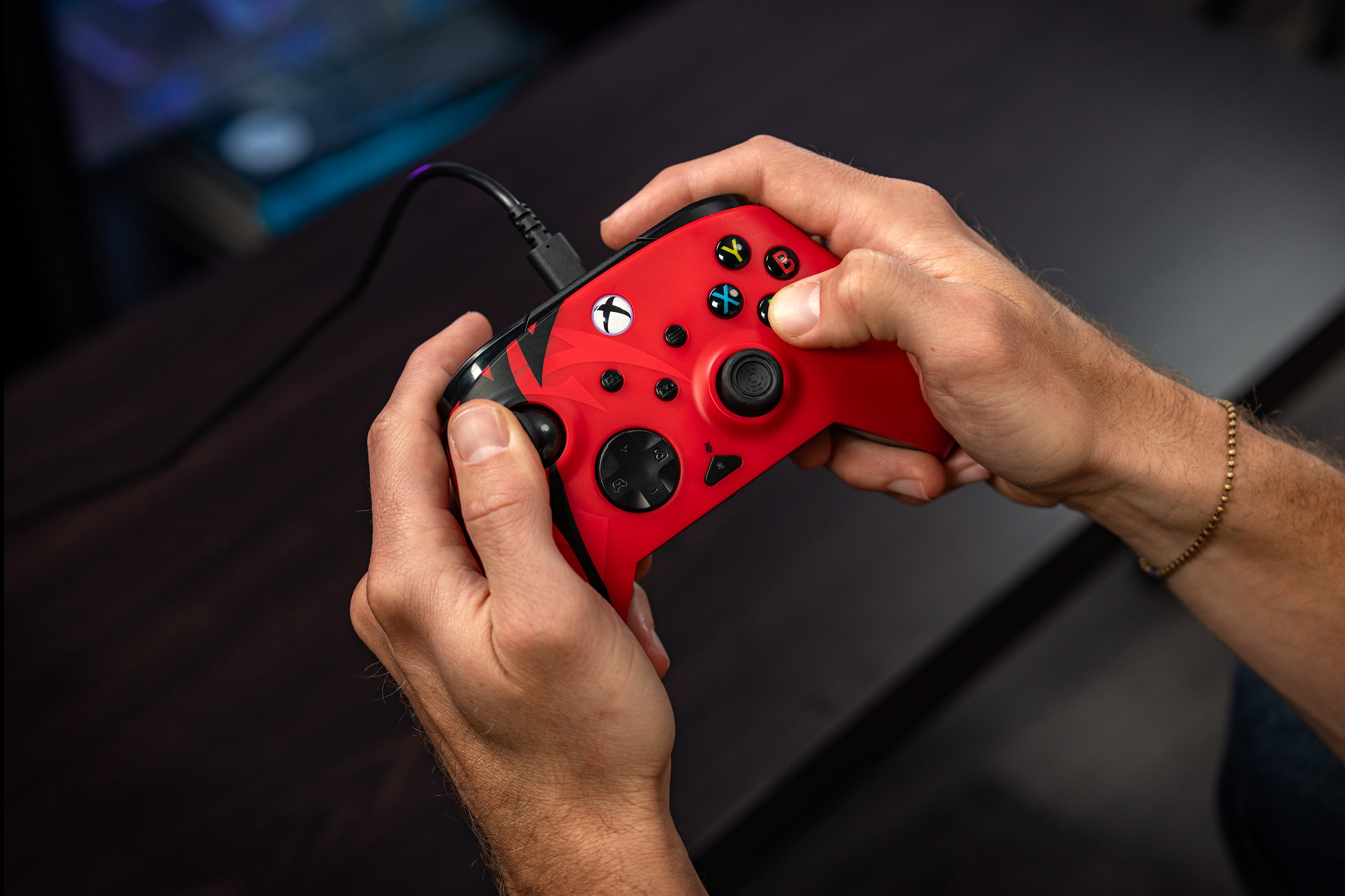Mains tenant une manette Xbox rouge avec des accents noirs sur fond sombre.