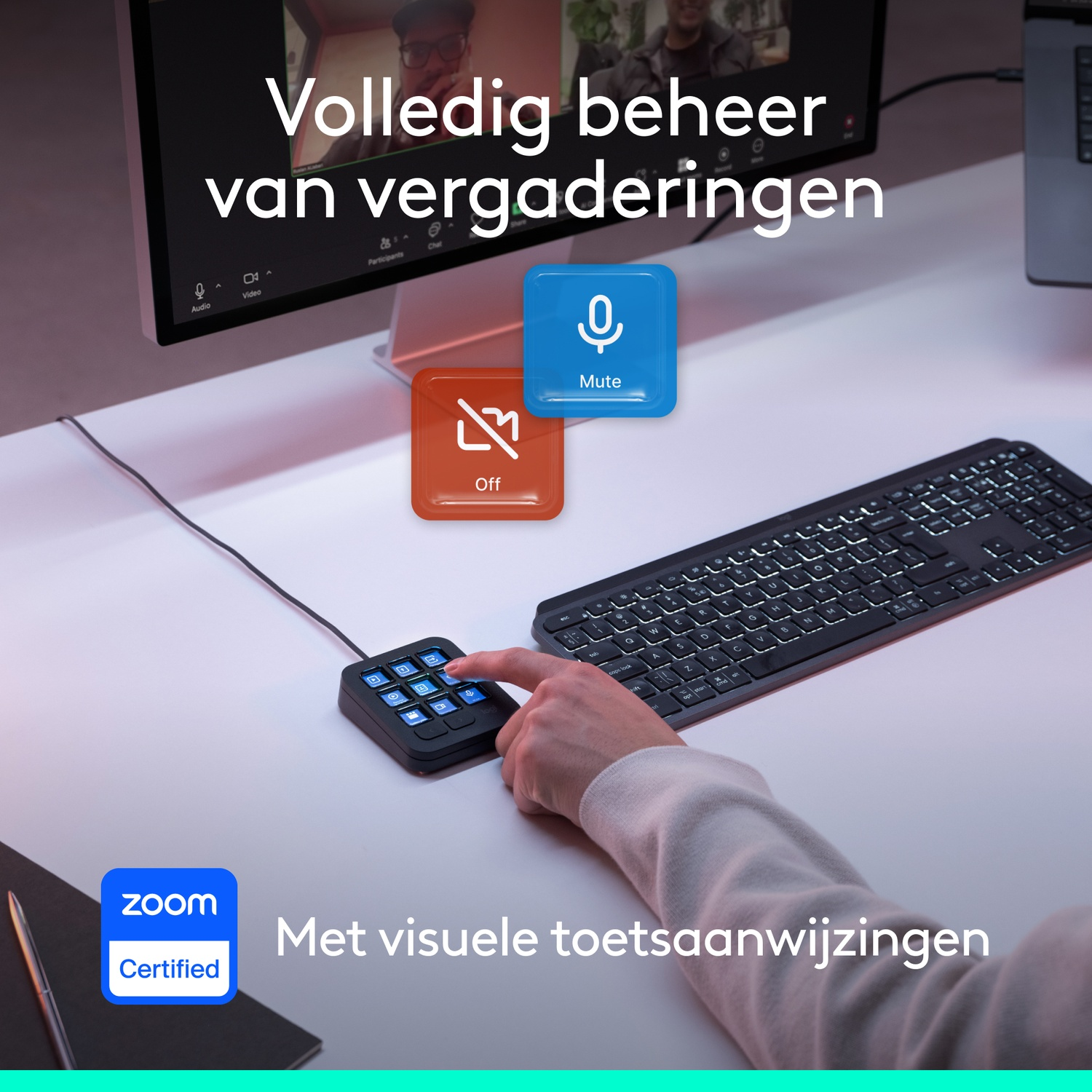 Hand drukt op een Logitech-toetsenbordcontroller met Zoom-pictogrammen, met monitor en toetsenbord.