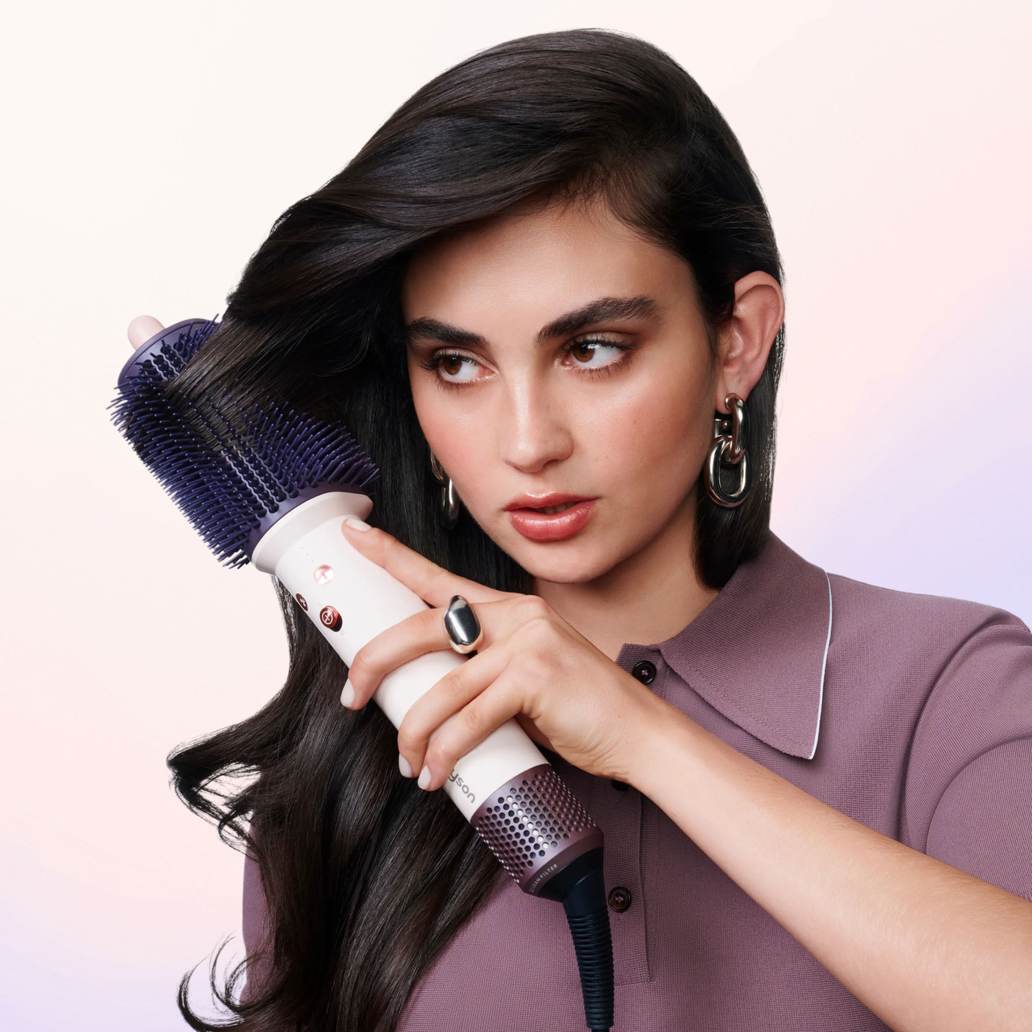 Een brunettemetaal met ringen style haar lange, donkere haar met een wit-paarse haarstijlbos tegen een roZE achtergrond.