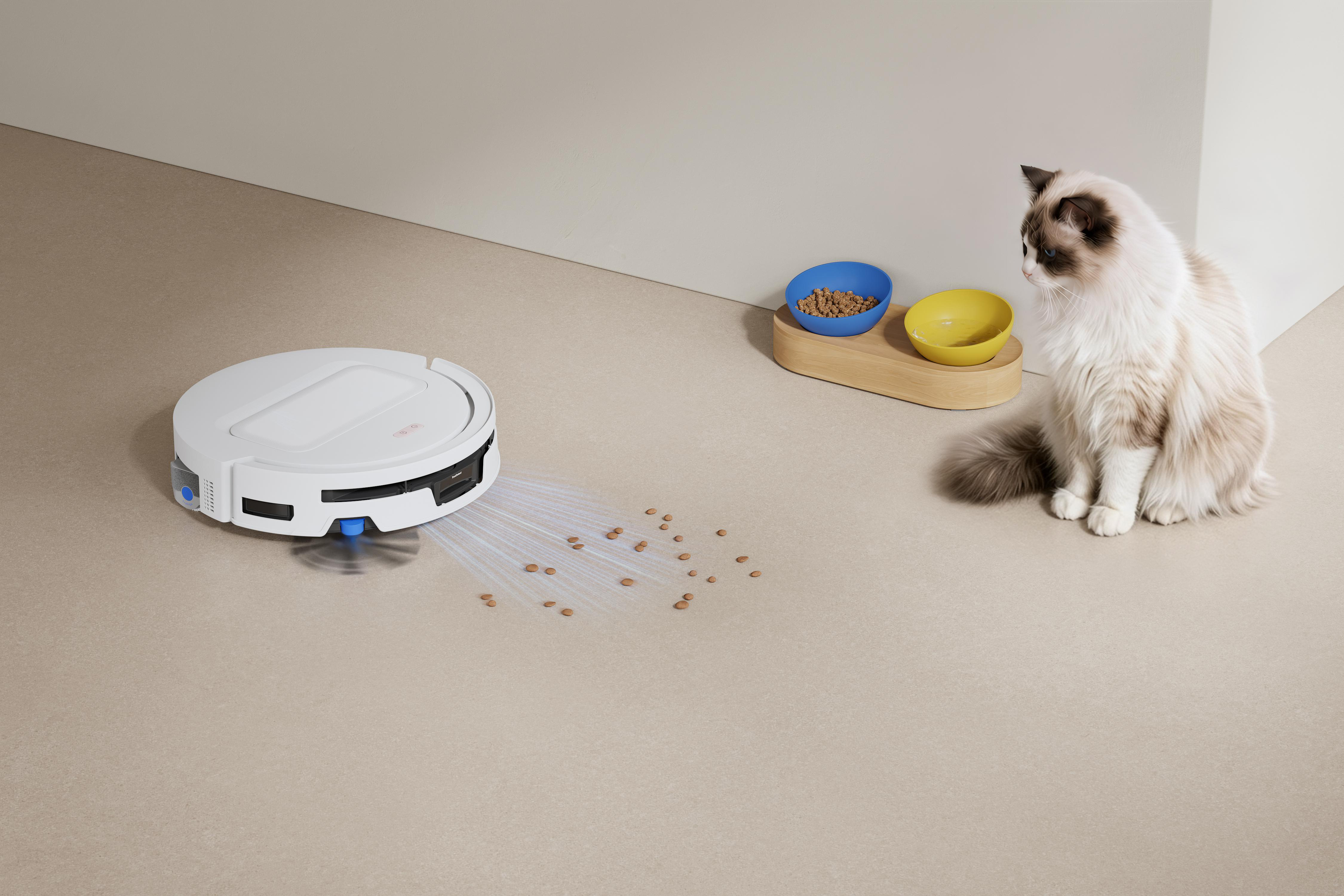 Ein weißer Saugroboter saugt Katzenfutter auf, während eine Katze daneben sitzt.