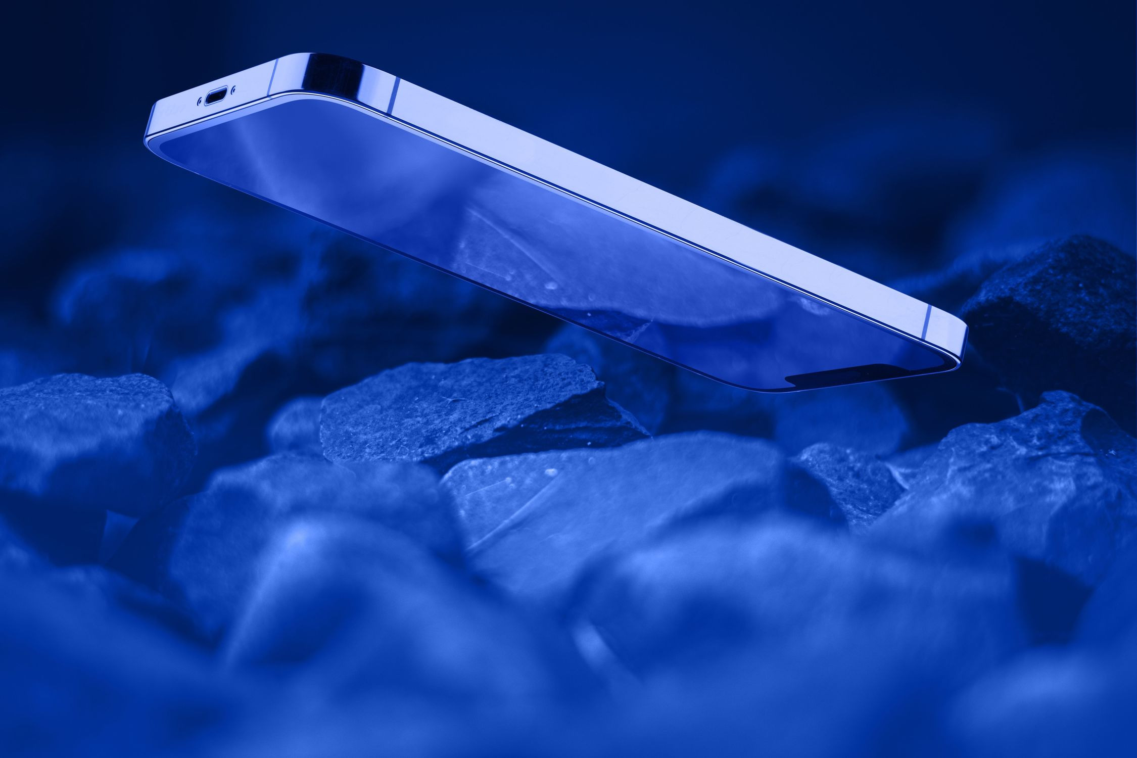 Un teléfono inteligente flota sobre rocas oscuras bajo luz azul.
