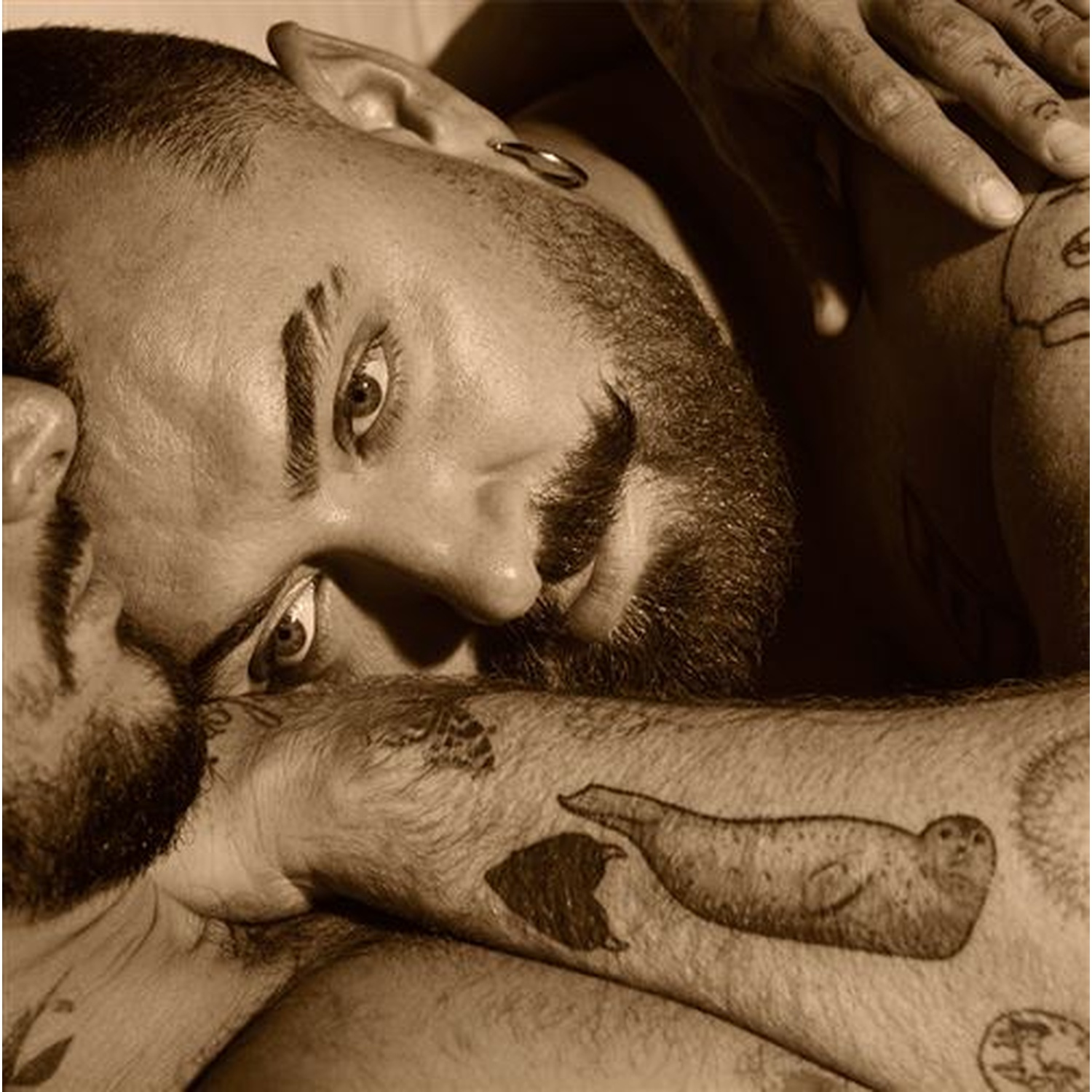 Gros plan d'un homme tatoué en sépia, se concentrant sur son visage et son bras.