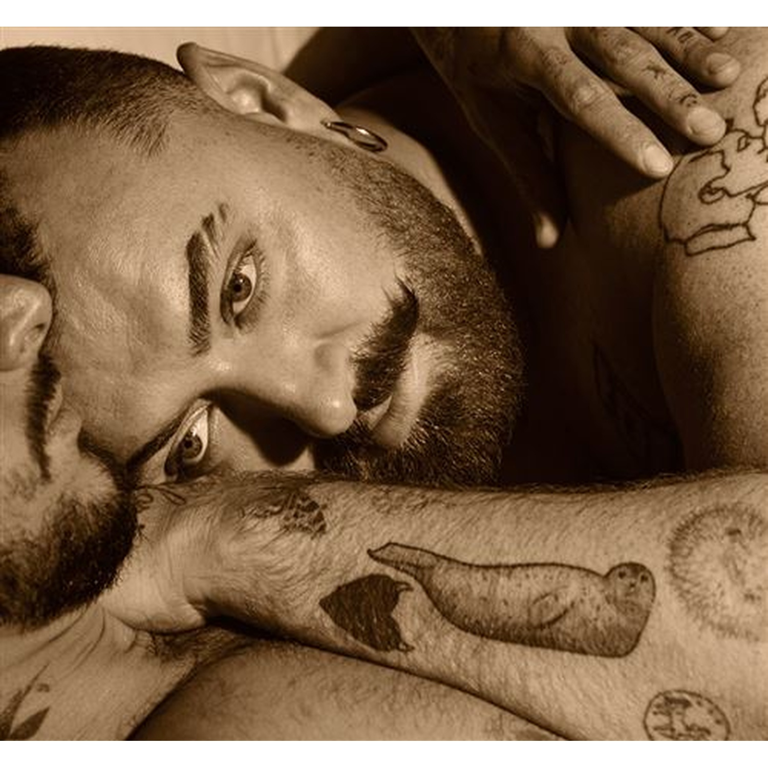 Gros plan sépia d'un homme tatoué allongé tout près d'une autre personne.