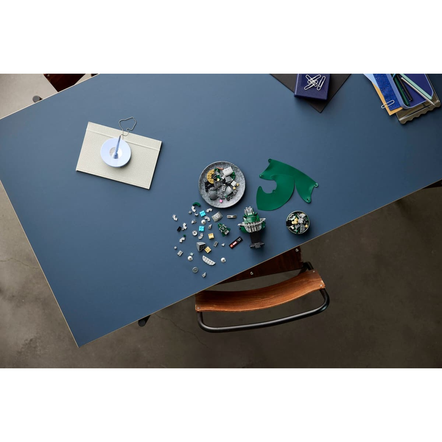 Vue plongeante d'une table bleue avec des pièces Lego, une cape verte, des bols et de la papeterie.
