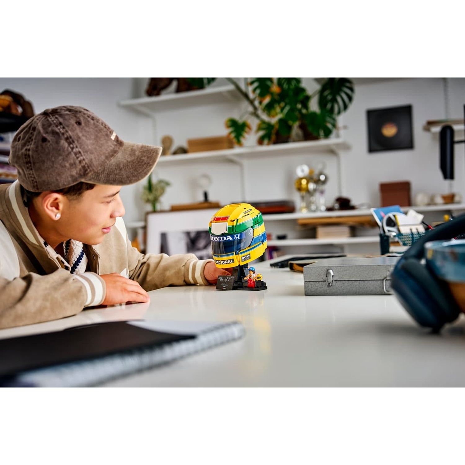 Un garçon portant une casquette regarde un casque de course Lego jaune et vert sur un bureau.