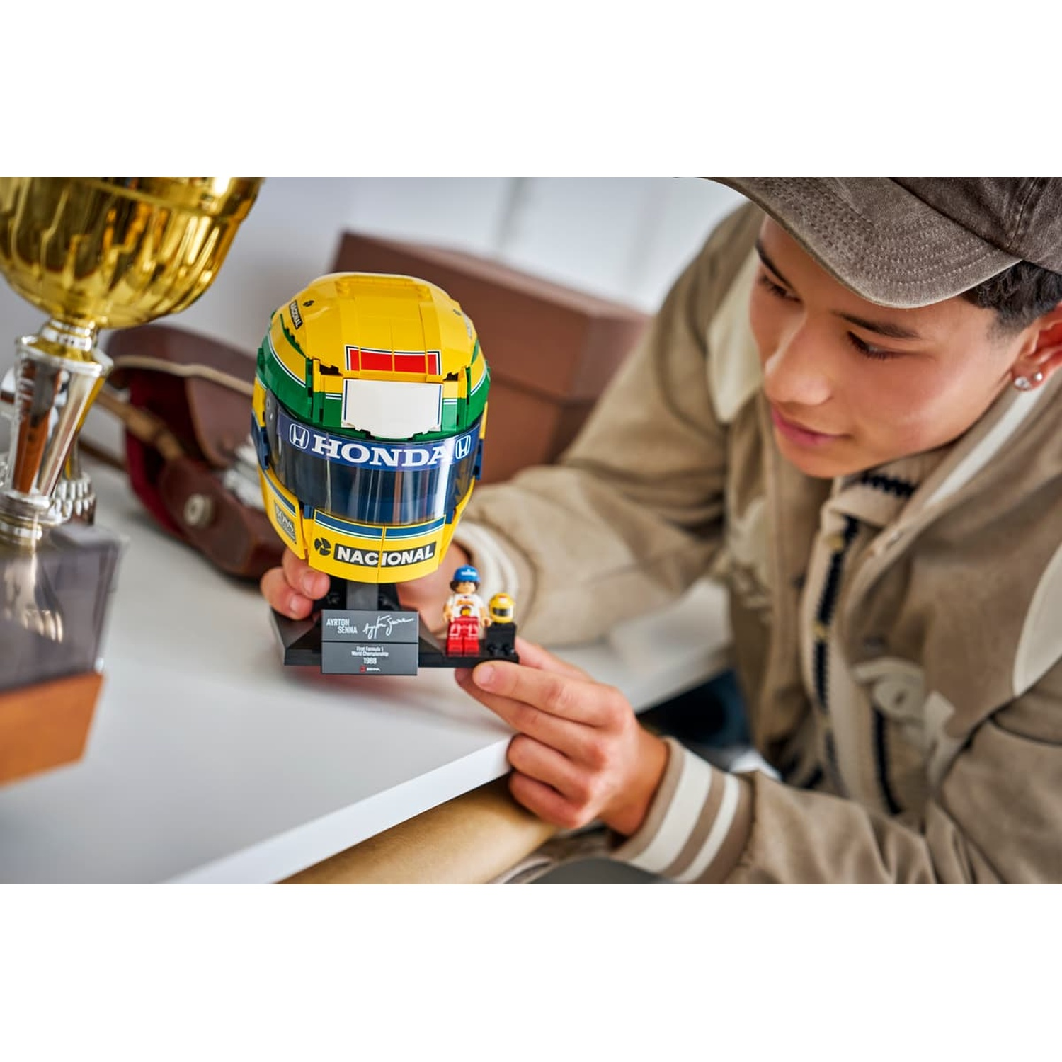 Un jeune homme tient un modèle de casque LEGO Ayrton Senna à côté d'un trophée doré.