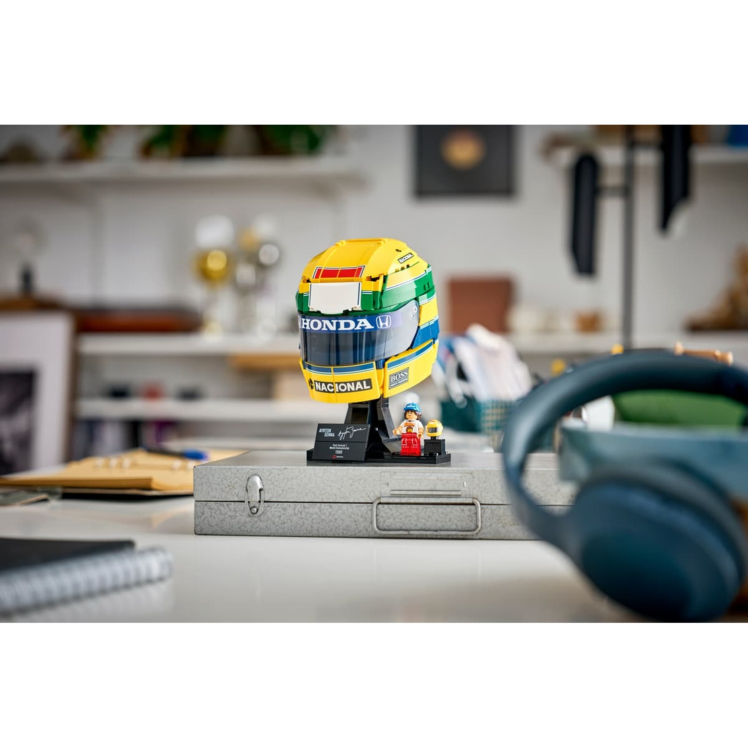 Un modèle Lego du casque de course jaune et vert d'Ayrton Senna est posé sur un étui métallique.