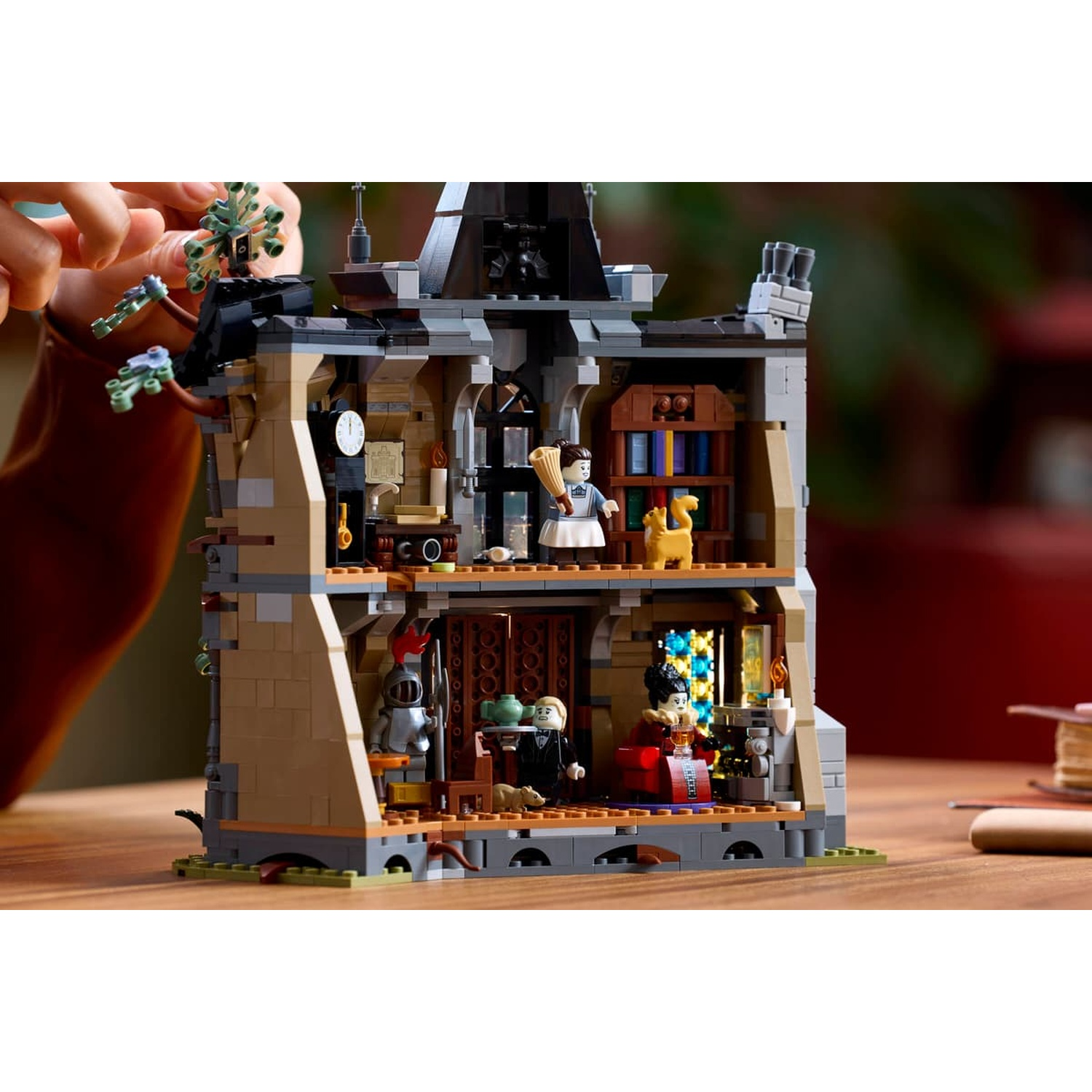 A detailed two-story LEGO mansion with various rooms, minifigures, and furniture on a wooden table.