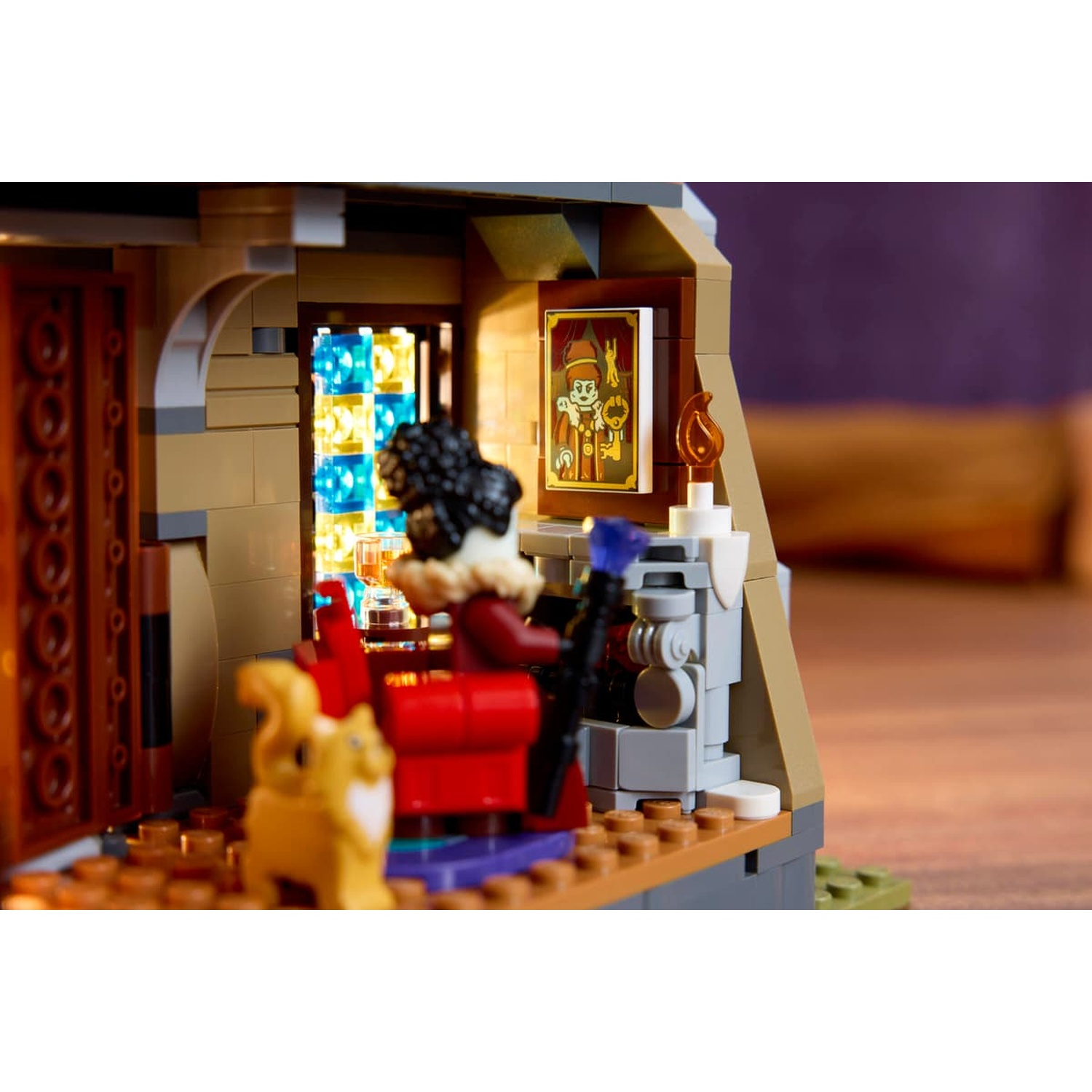 A Lego minifigure sits in a red chair with a cat, near a fireplace and a framed picture on the wall.