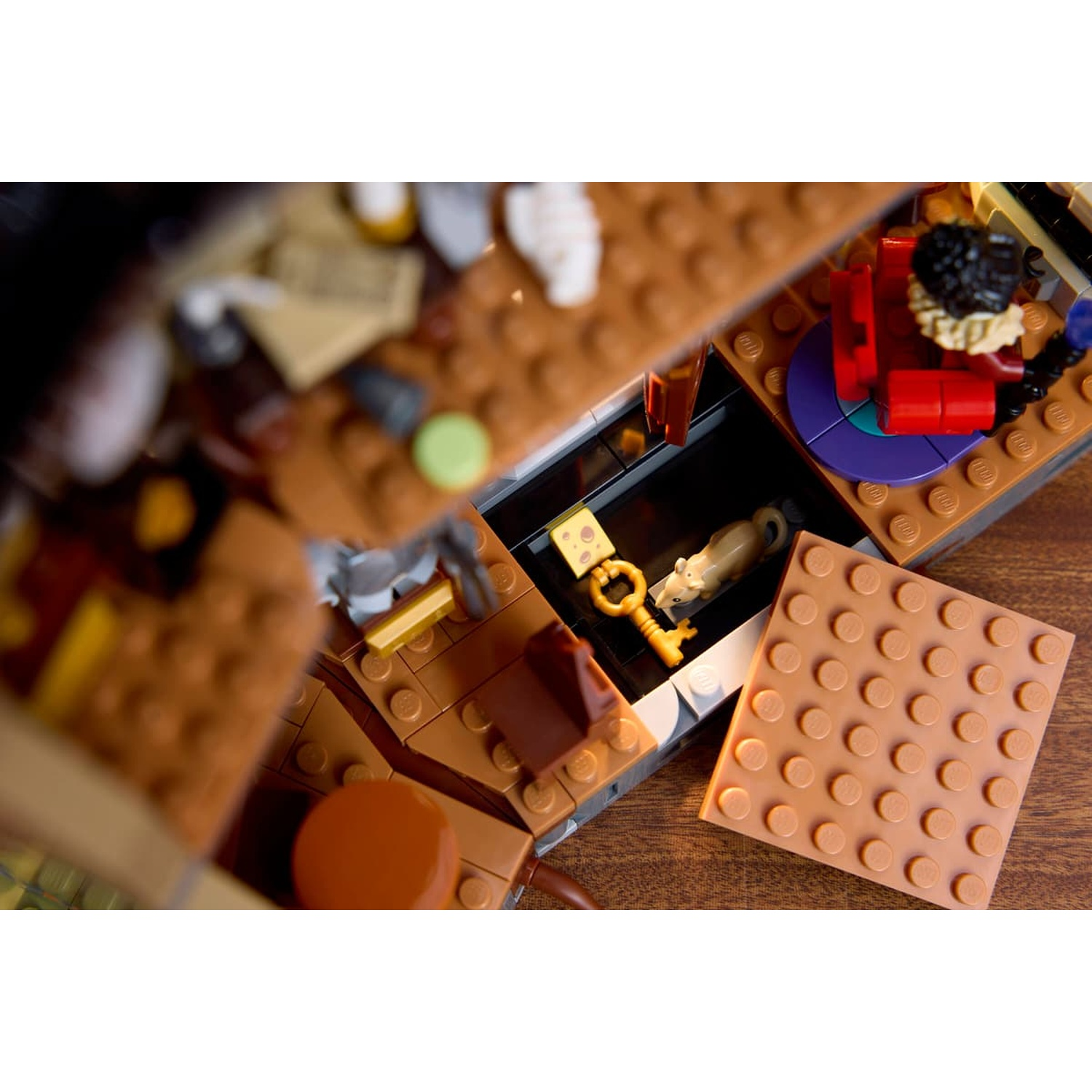 Top view of a Lego room showing a rat, cheese, key, and a detached brown plate cover on a wooden surface.