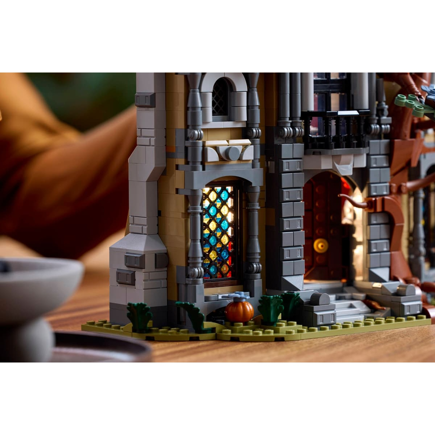Detailed view of a LEGO mansion with a stained glass window, pumpkin, and lit entrance.