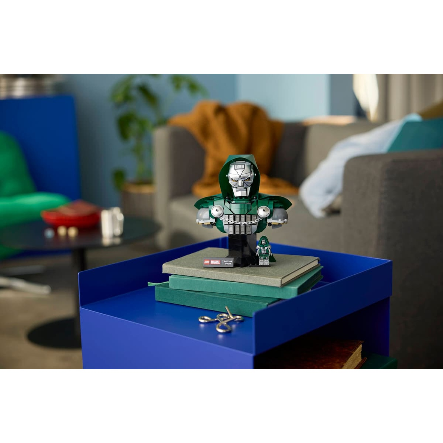 Un buste Lego de Docteur Doom posé sur des livres verts sur une table bleue.