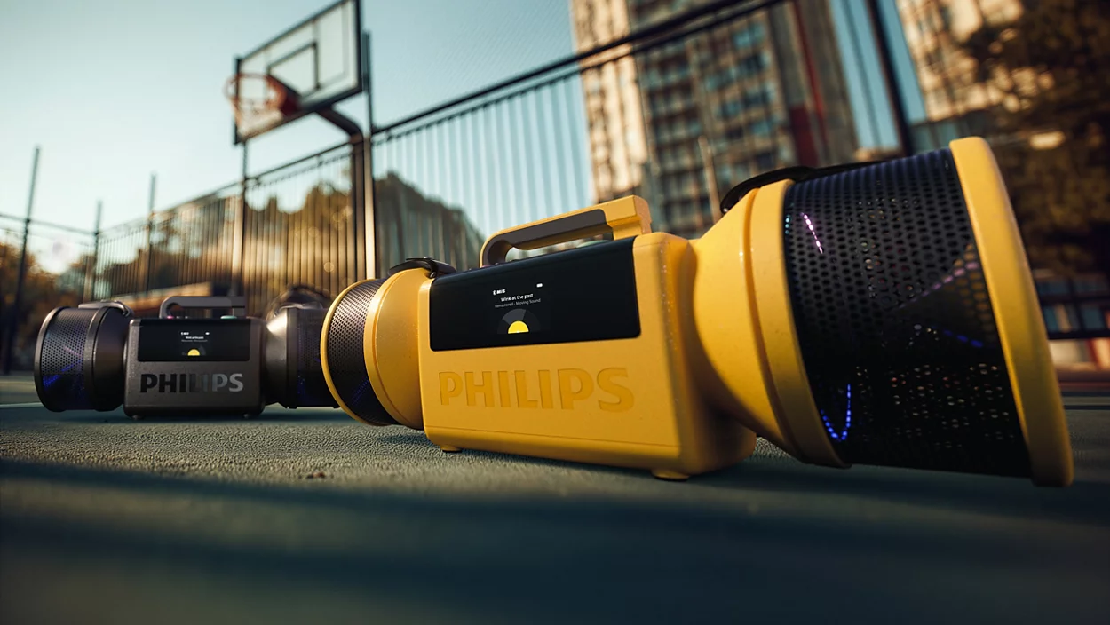Egy élénksárga hordozható Philips hangszóró egy kosárpályán, mögötte egy kisebb feketével.