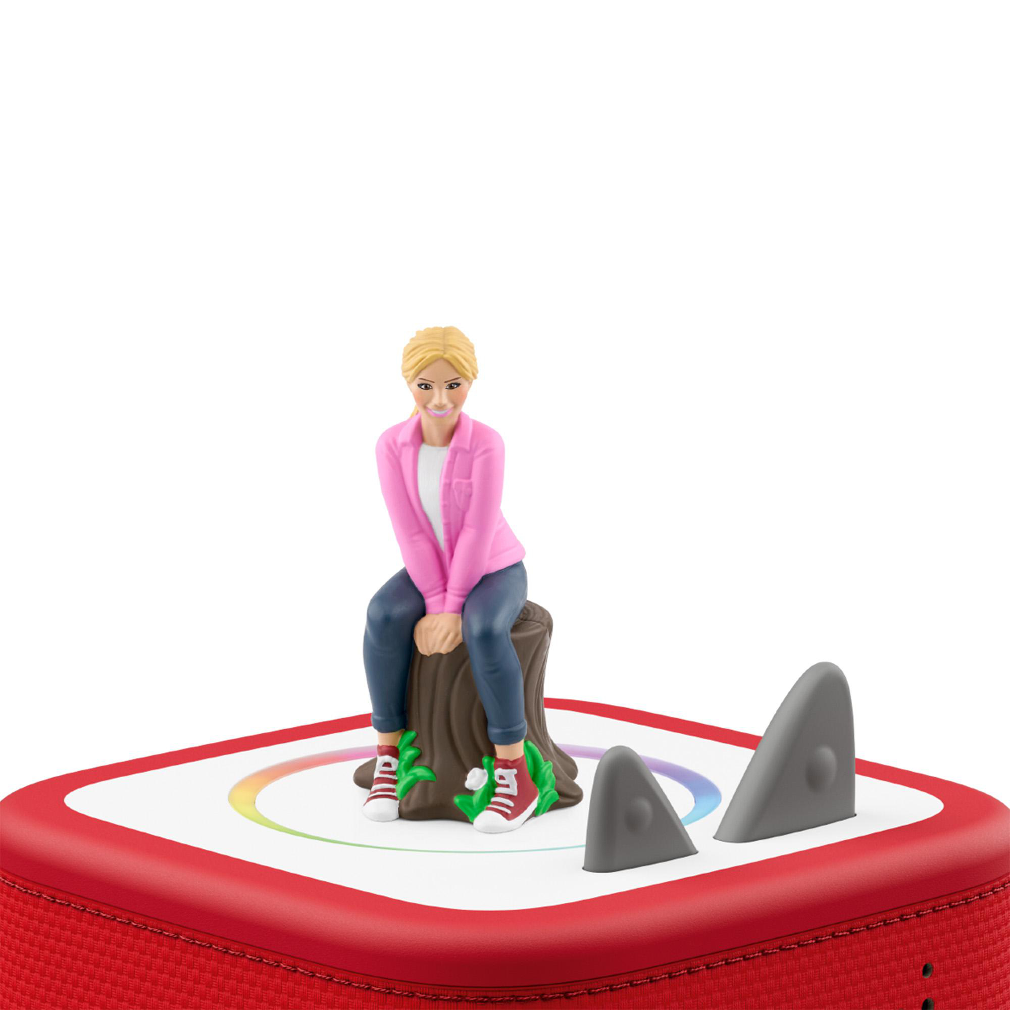 Eine blonde Spielfigur in rosa Jacke sitzt auf einem Baumstamm auf einem rot-weißen Lautsprecher.