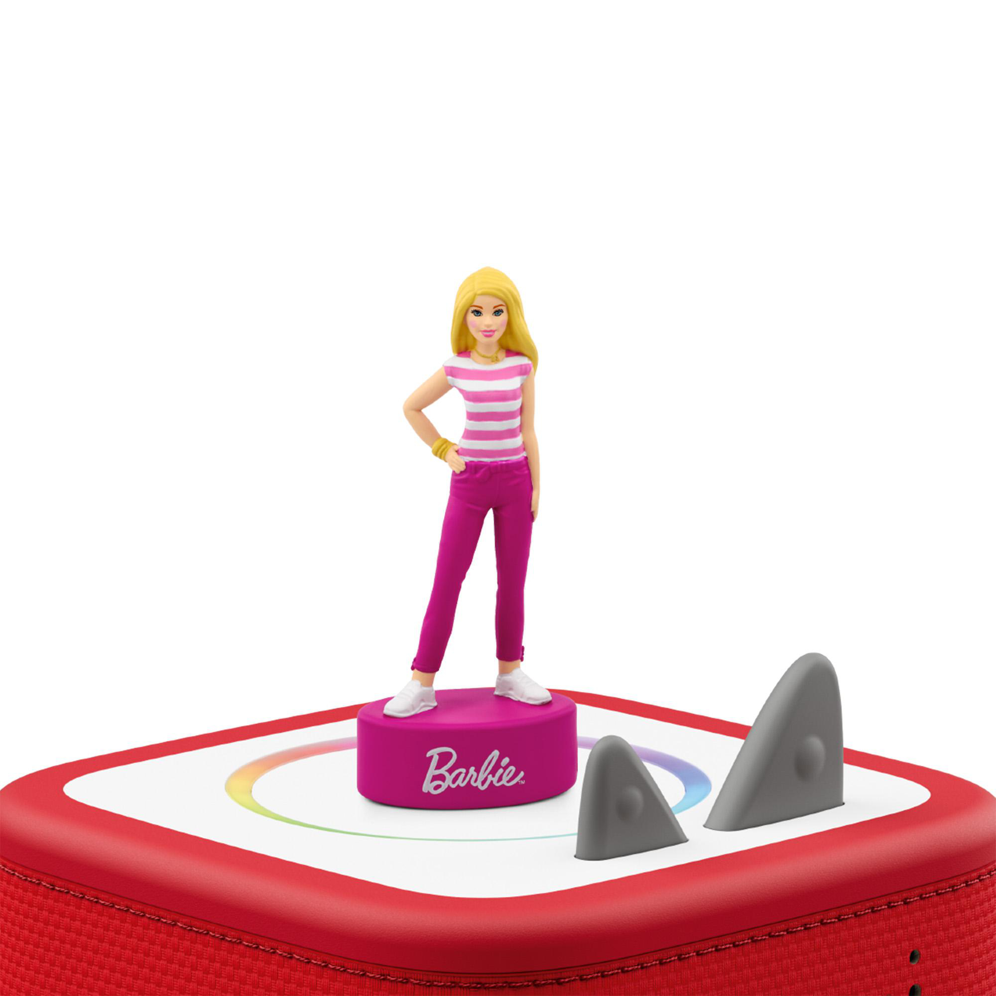 Eine Barbie-Figur in rosa-weißer Kleidung steht auf einem roten Sockel mit Aufschrift, neben zwei grauen Haifischflossen.