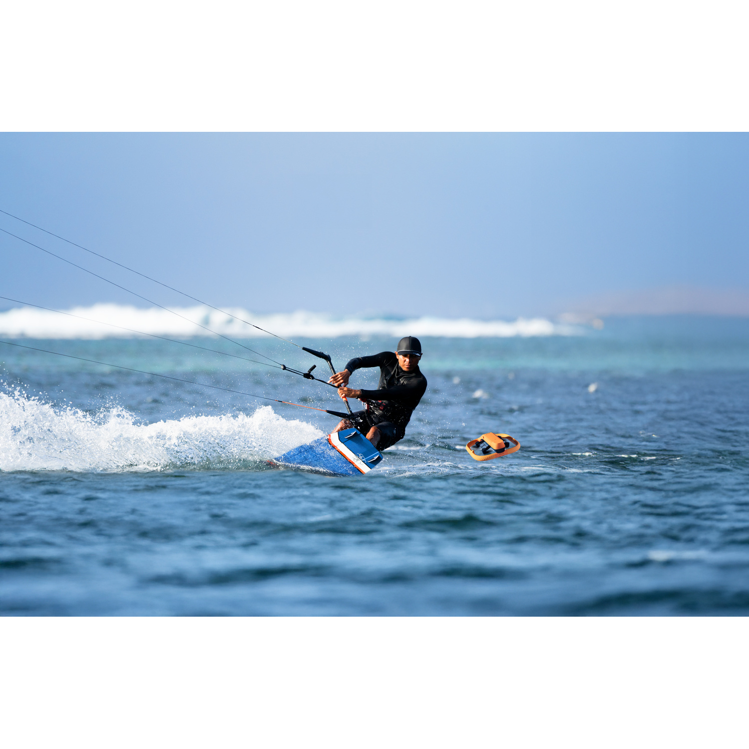 Un kitesurfer in muta nera cavalca una tavola blu sull'acqua turchese.