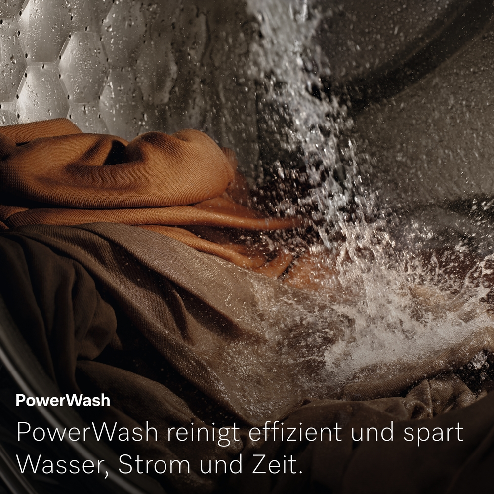 Wasser spritzt in einer Waschmaschinentrommel auf braune Kleidung.
