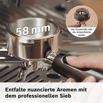 Ein 58mm Espressosiebhalter mit schwarzem Griff wird in einer Hand gehalten, im Hintergrund eine Kaffeemaschine.