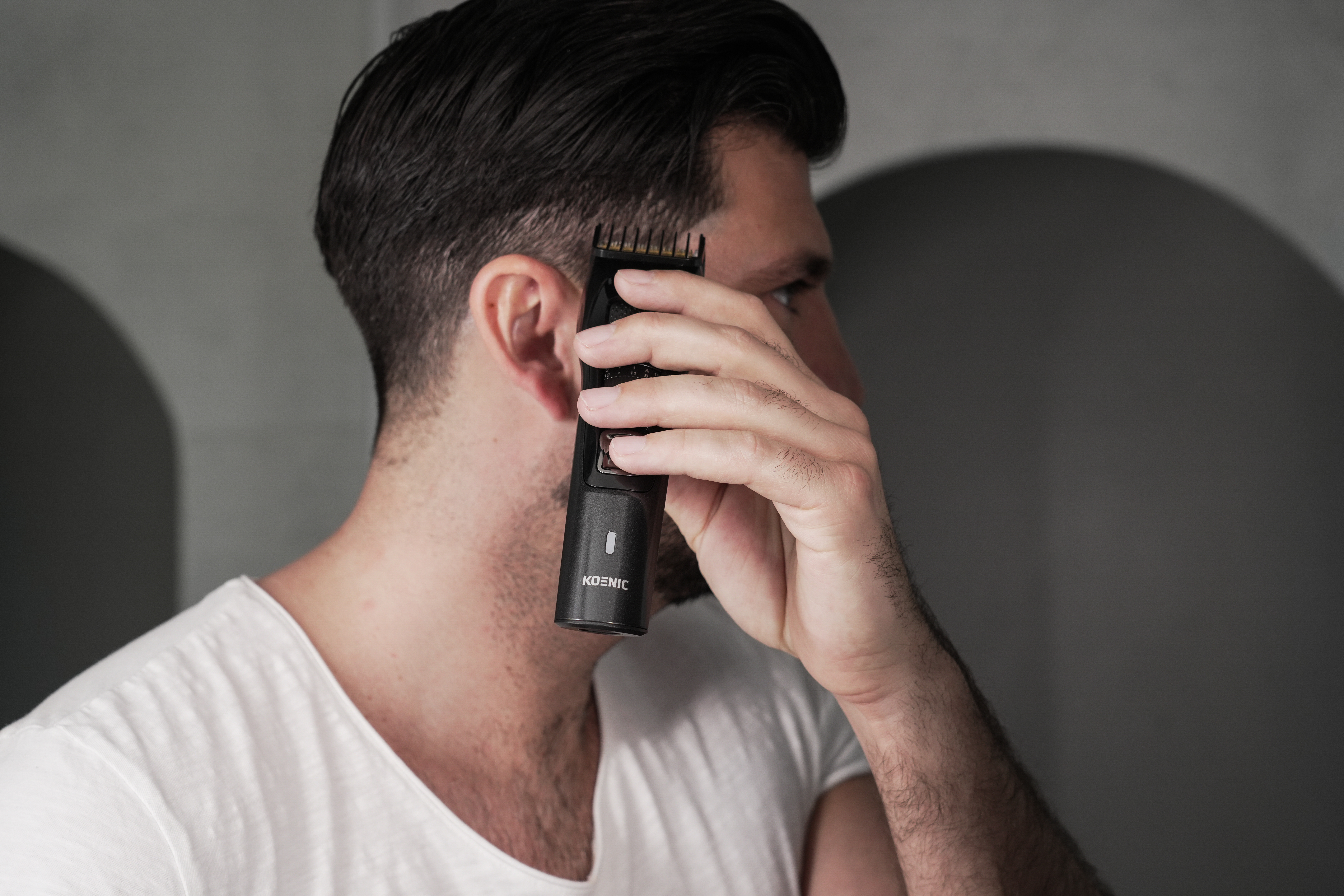 Ein Mann schneidet sich mit einem schwarzen Haarschneider der Marke KOENIC die Haare an der Seite.