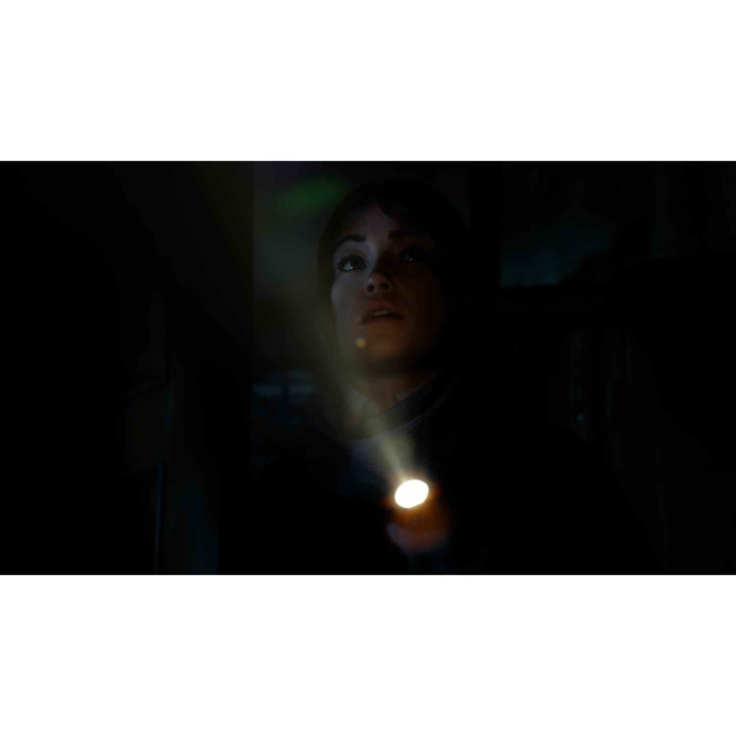 Una scena buia e poco illuminata mostra una donna che tiene una piccola torcia, illuminando il suo viso dal basso.