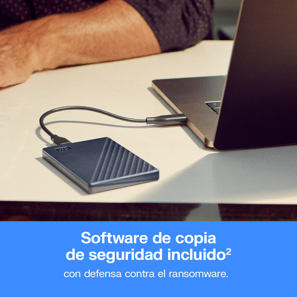 Un disco duro externo conectado por cable a una laptop en una mesa clara.