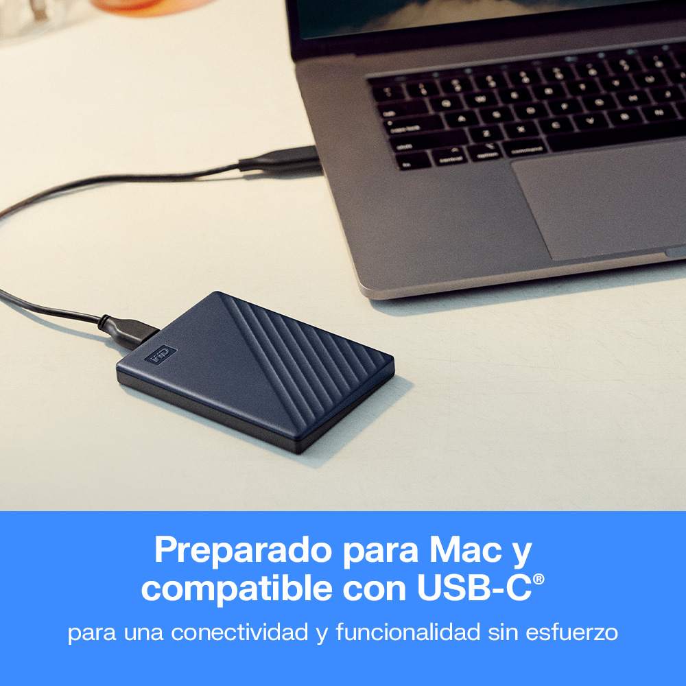 Un disco duro externo azul está conectado por cable a un portátil gris en un escritorio blanco.