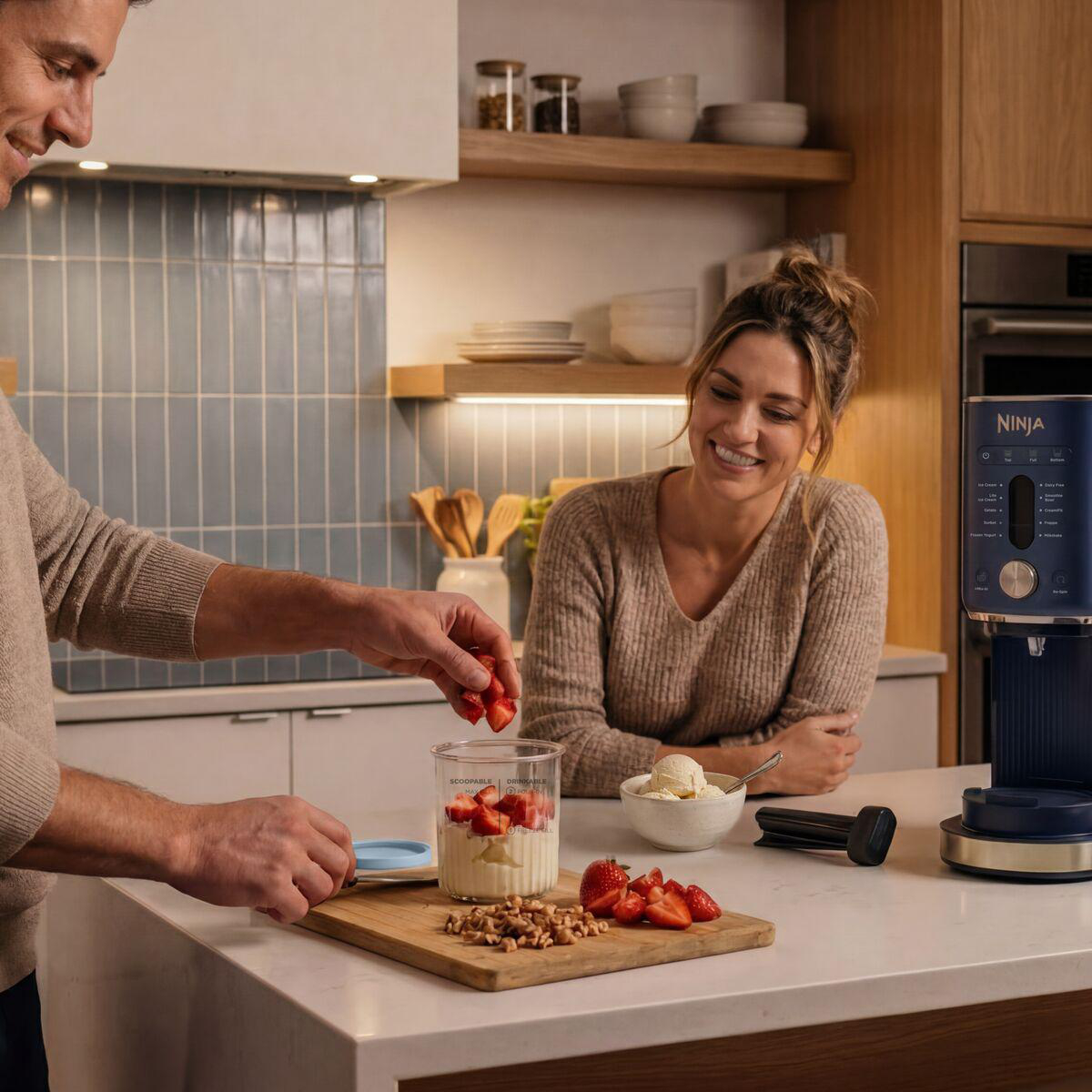 Ein Mann fügt Erdbeeren zu einem Dessert hinzu, während eine Frau in einer modernen Küche zusieht.