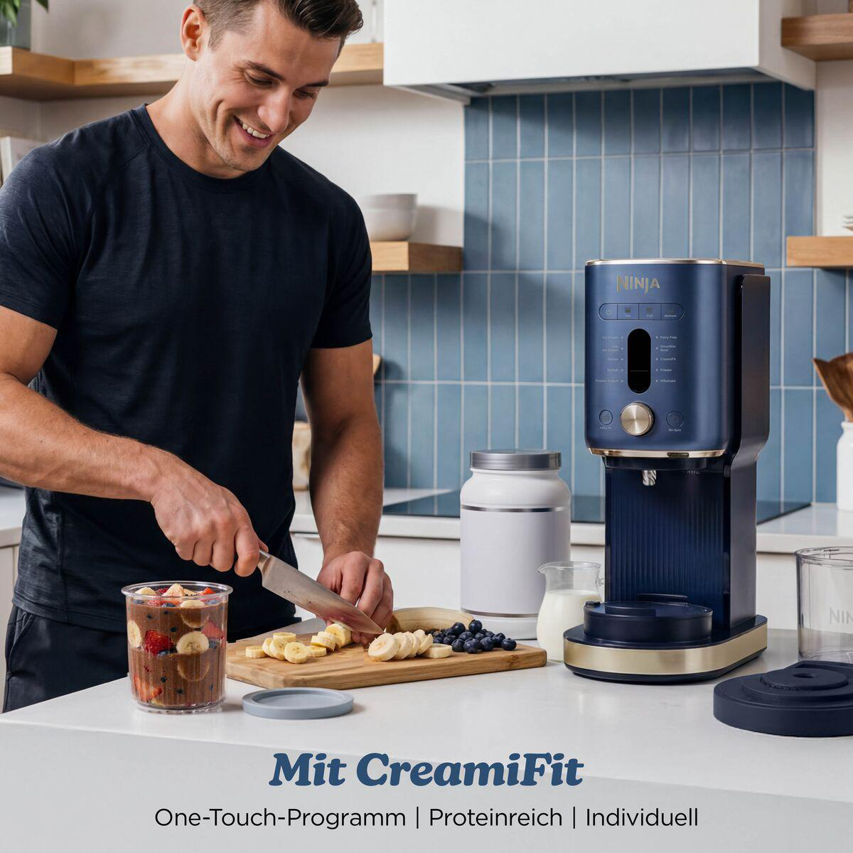 Ein Mann schneidet Bananen auf einem Brett in einer Küche neben einer blauen Ninja-Eismaschine.