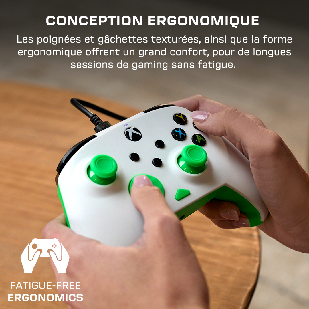 Une personne tient une manette Xbox blanche et verte sur une surface en bois.