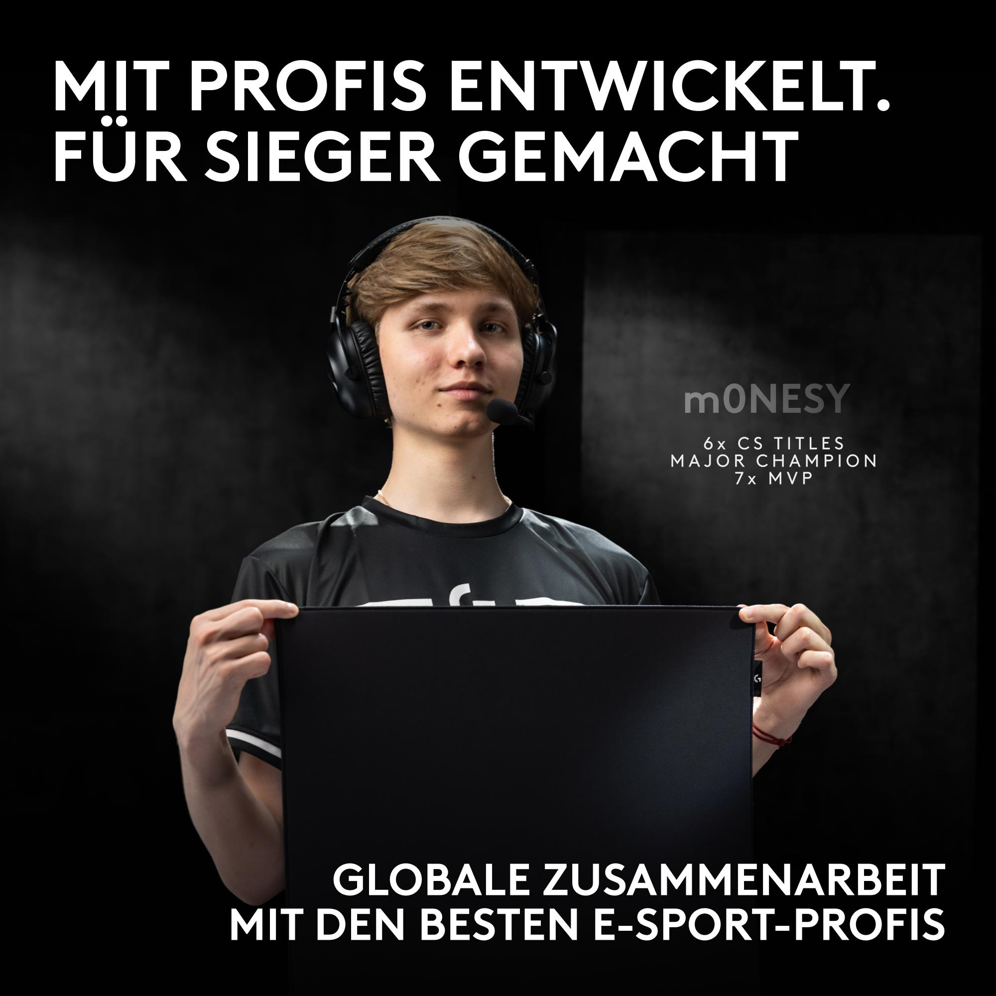 Junger E-Sportler mit Headset hält ein großes schwarzes Mauspad vor dunklem Hintergrund.
