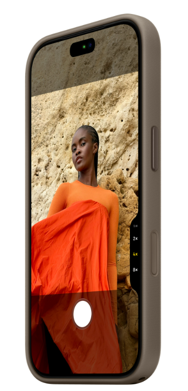 Smartfon wyświetlający widok aparatu z kobietą w pomarańczowym ubraniu przed ścianą skalną.