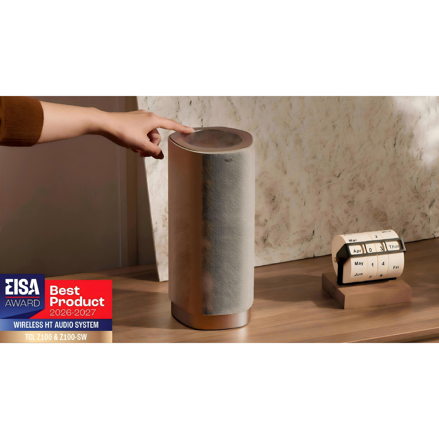 Mano che tocca un altoparlante cilindrico su un tavolo di legno con calendario e badge EISA.