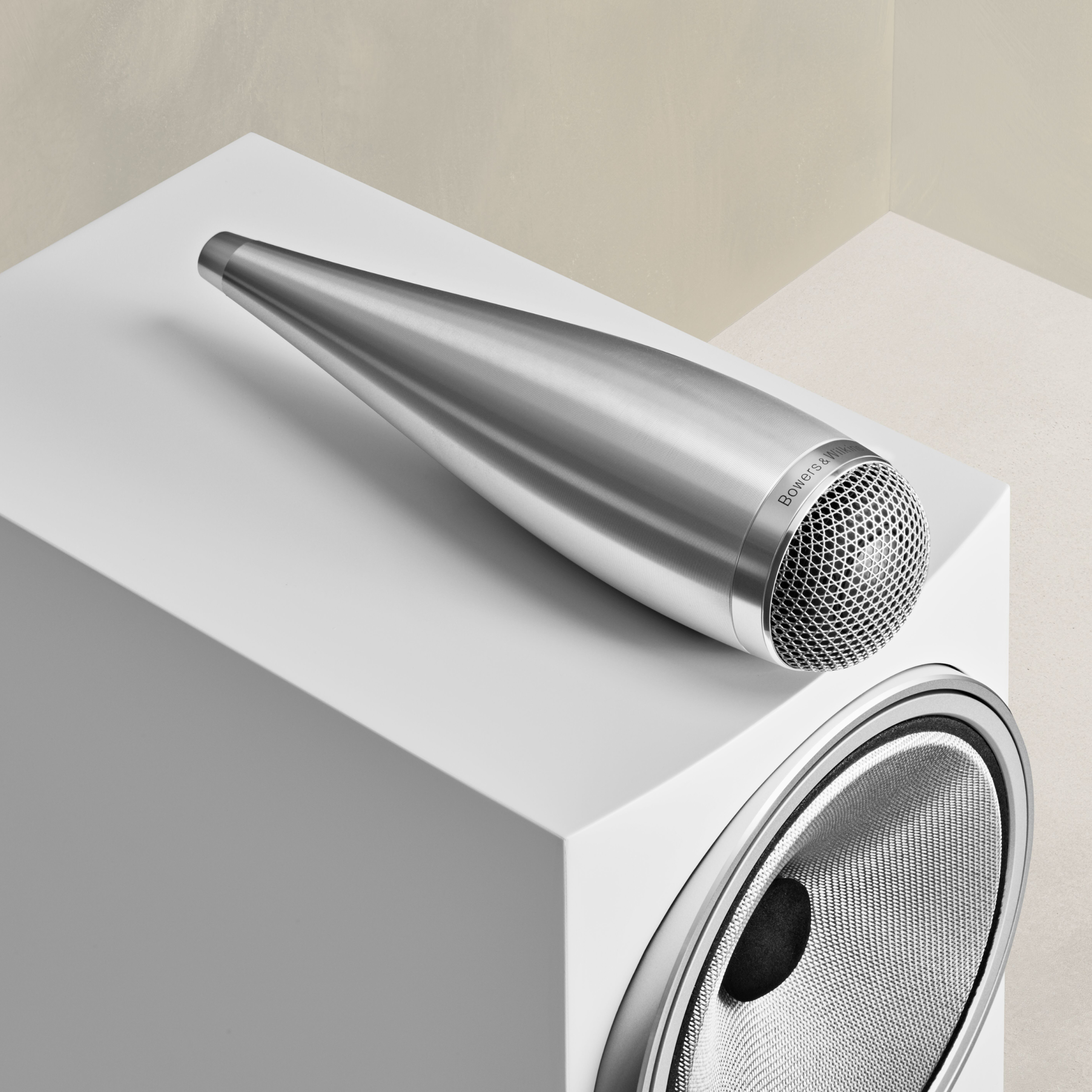 Ein silberner, kegelförmiger Lautsprecher liegt auf einem großen, weißen Subwoofer mit einem Metallgitter.