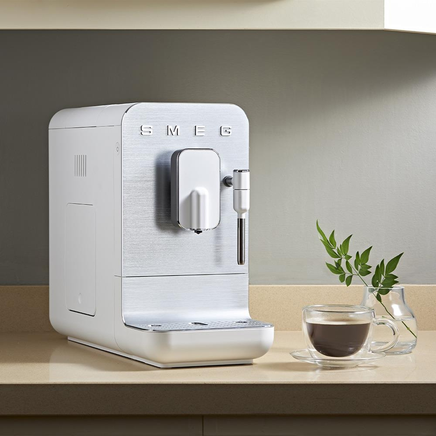 Una macchina da caffè SMEG bianca si trova su un bancone da cucina vicino a una tazza di caffè.