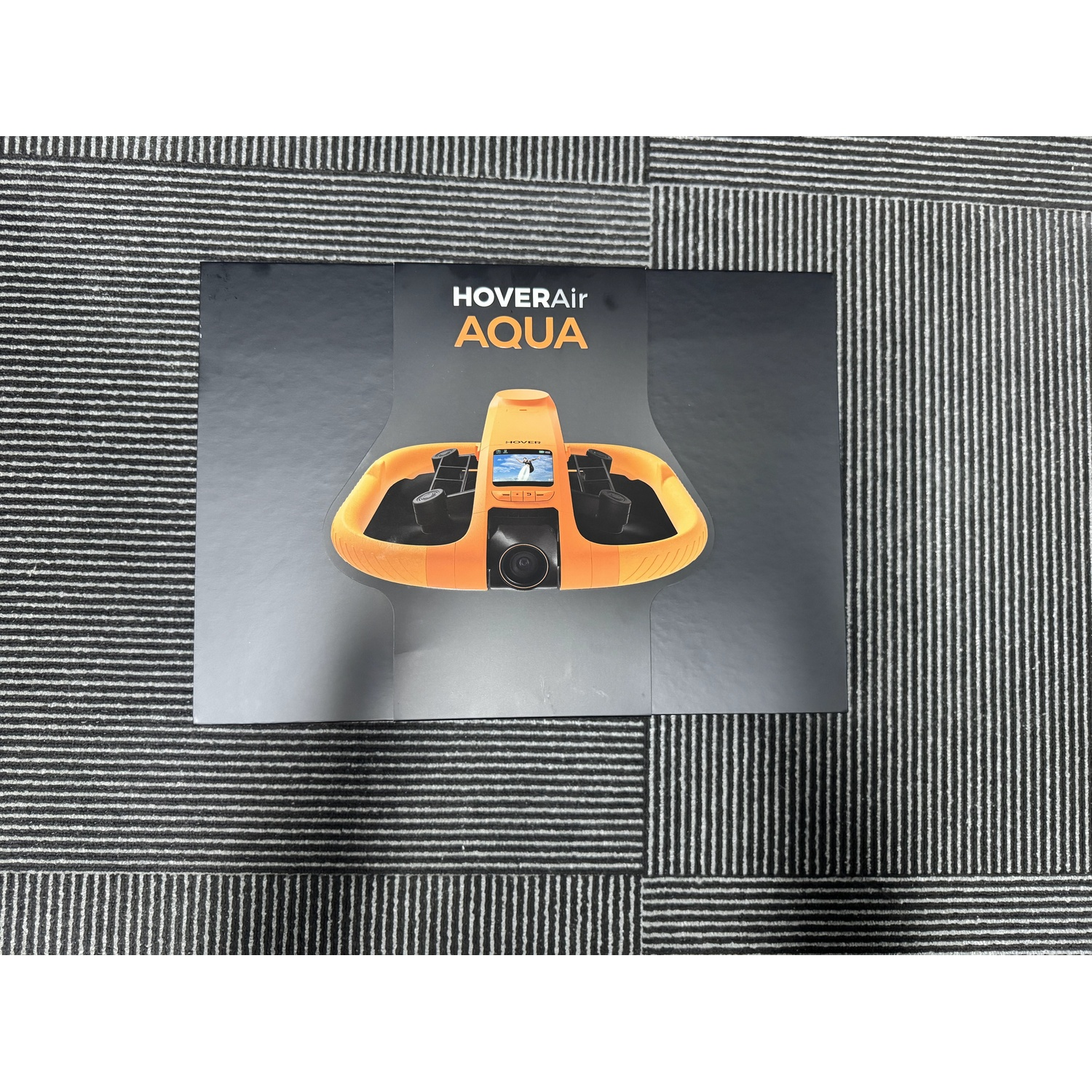 Scatola nera per il drone subacqueo HoverAir Aqua giallo su sfondo a righe grigie e nere.