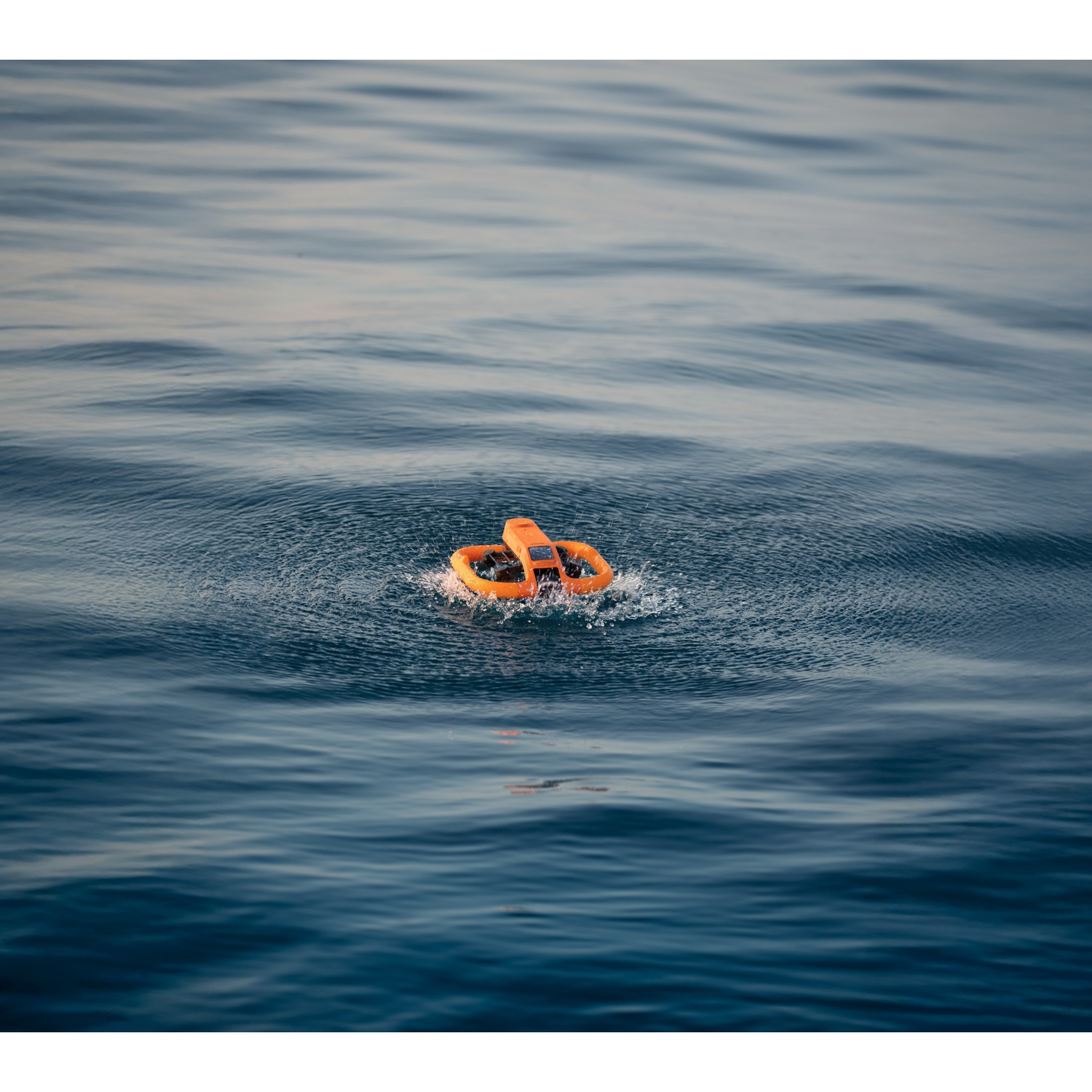 Un drone telecomandato arancione galleggia sul mare blu aperto, creando piccole onde.