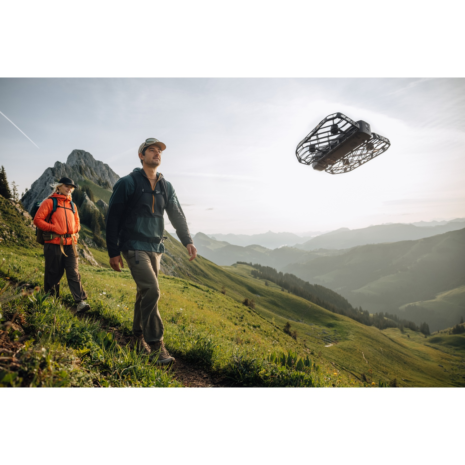 Escursionisti su un sentiero di montagna guardano un drone con telecamera con montagne distanti.