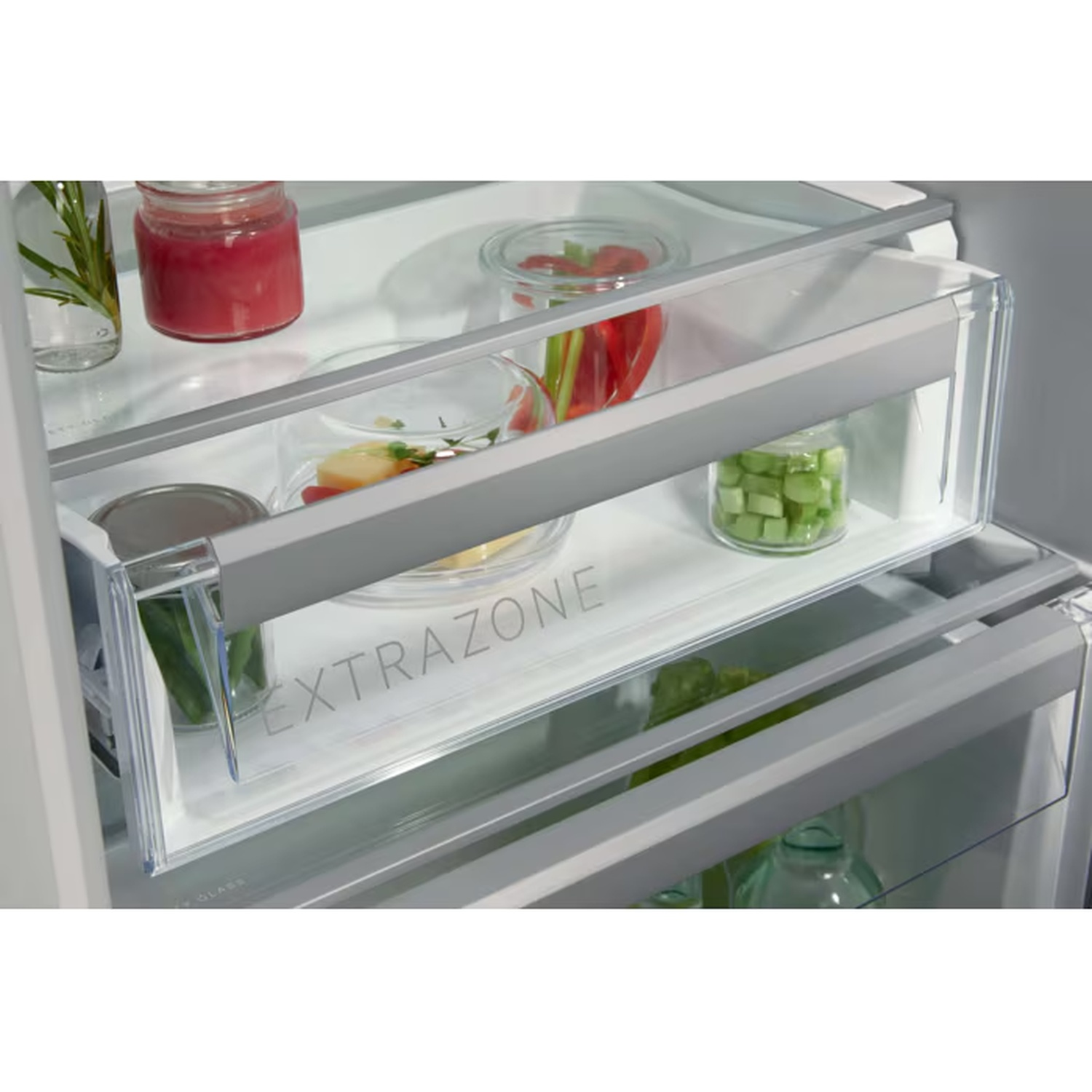 Inside view of a refrigerator with organized glass shelves and transparent ExtraZone drawers containing jars and fresh food.