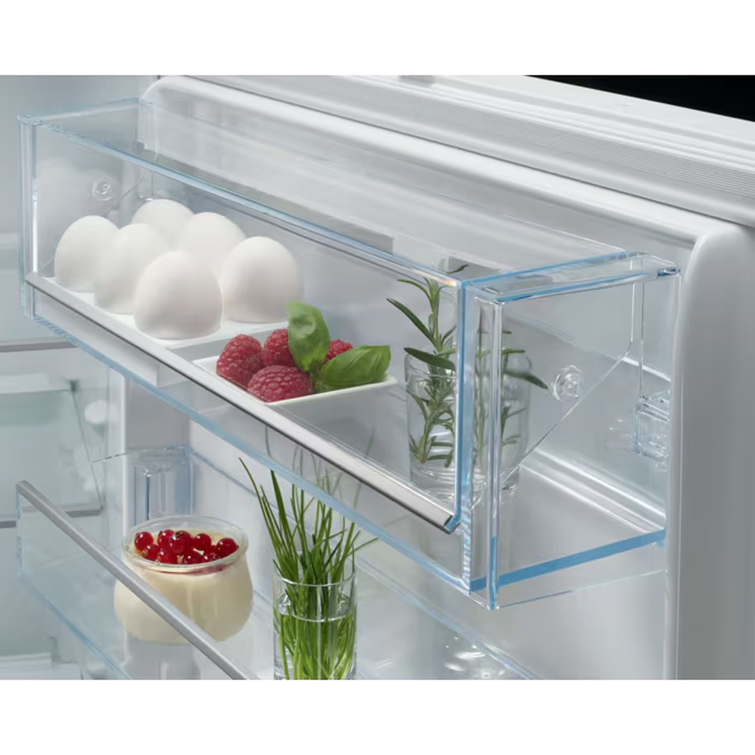 Open refrigerator door filled with eggs, raspberries, rosemary, chives, and yogurt.