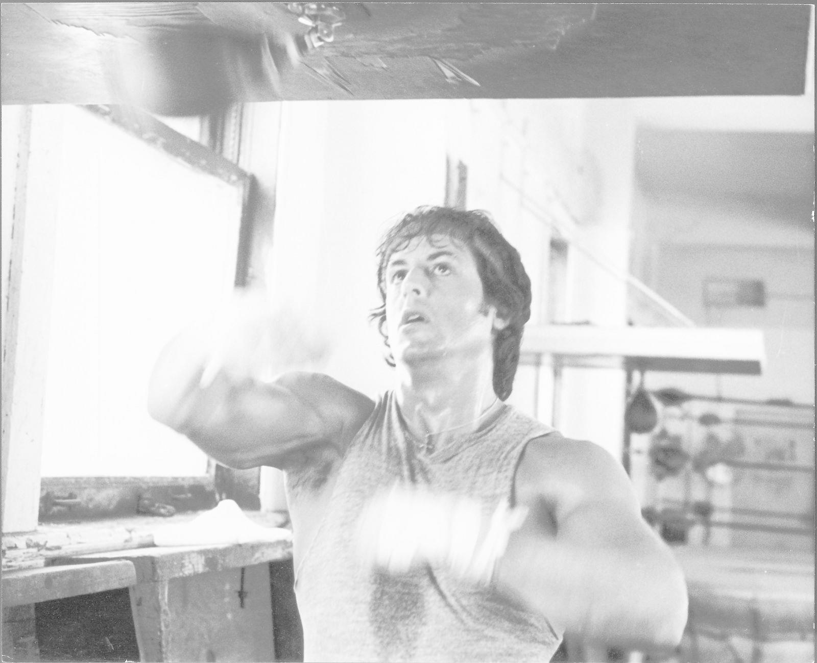 Ein Schwarz-Weiß-Foto eines Mannes in einem Tanktop, der in einem Fitnessstudio gegen einen Punchingball schlägt.